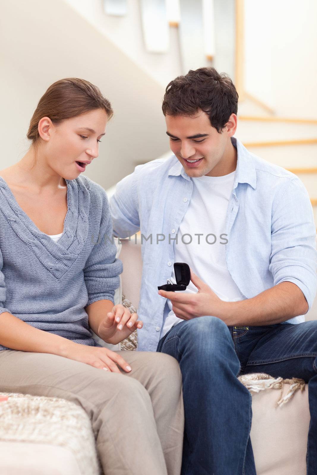 Portrait of a man offering a ring to her girlfriend in their living room