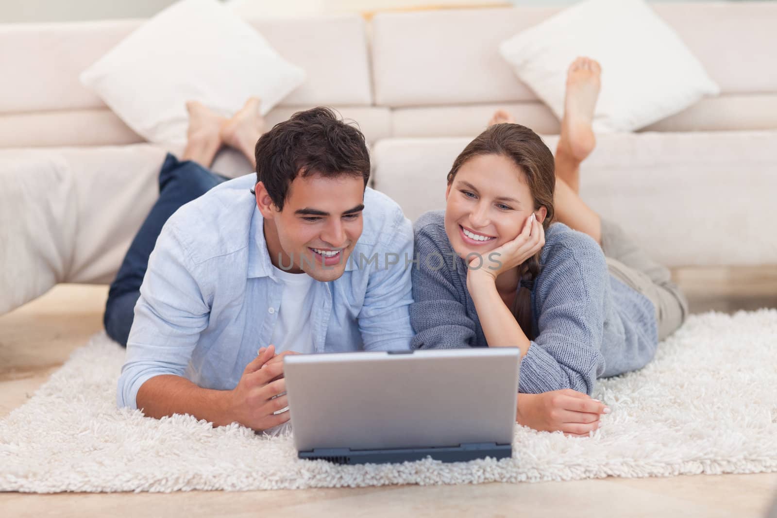 Young couple looking for something on the internet while lying on a carpet
