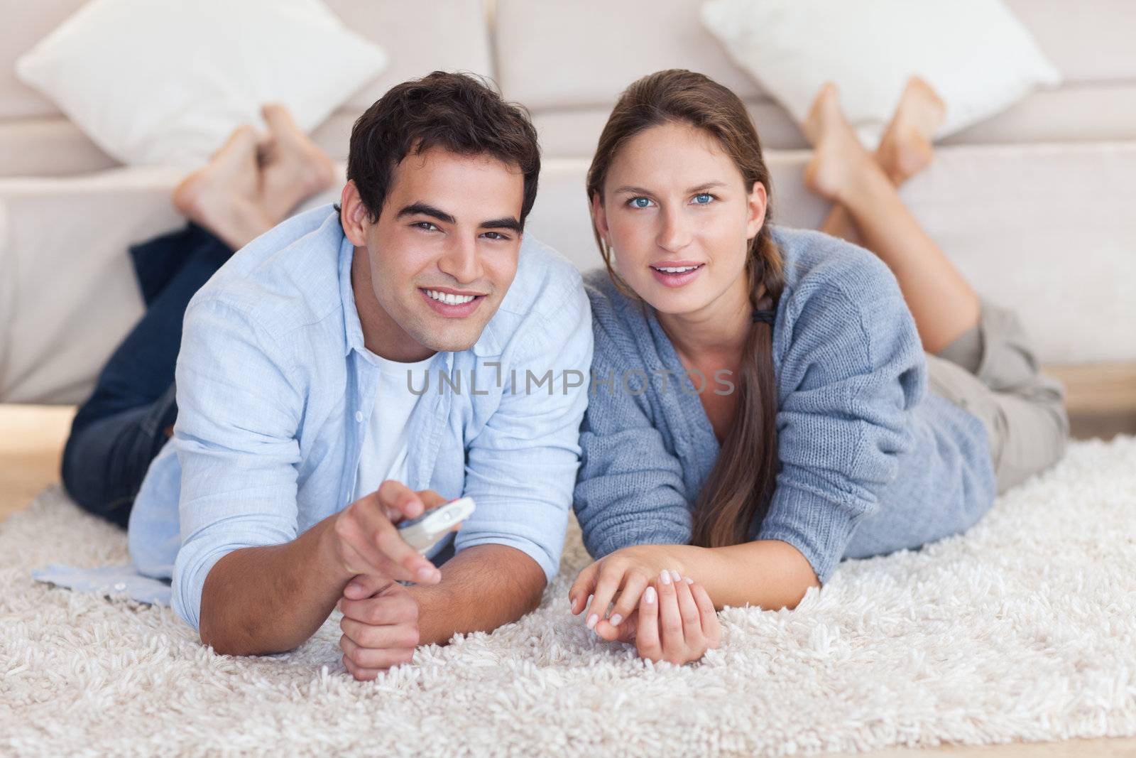 Lovely couple watching TV while lying on a carpet in their living room