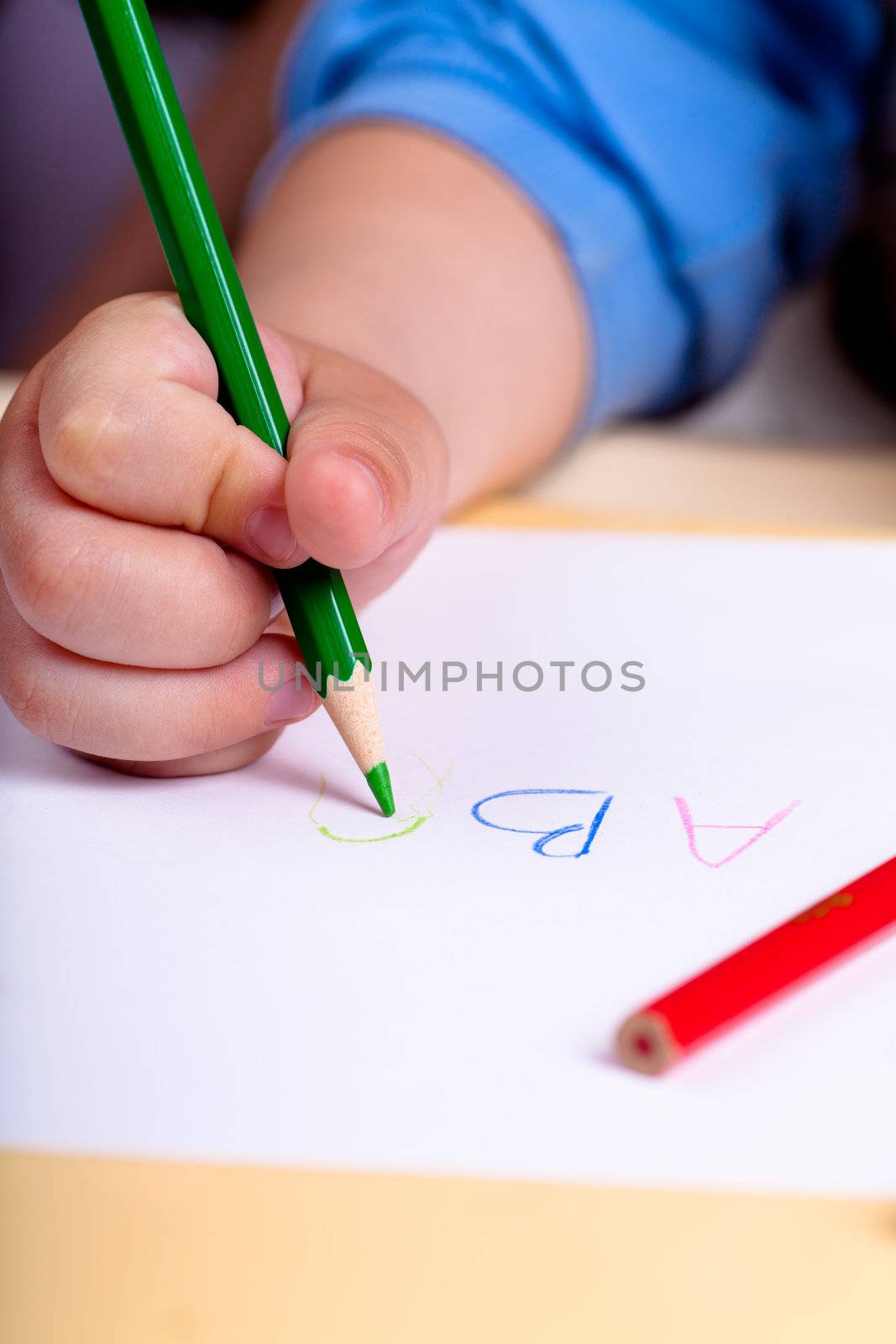Child's hand writing letters with gree pencil