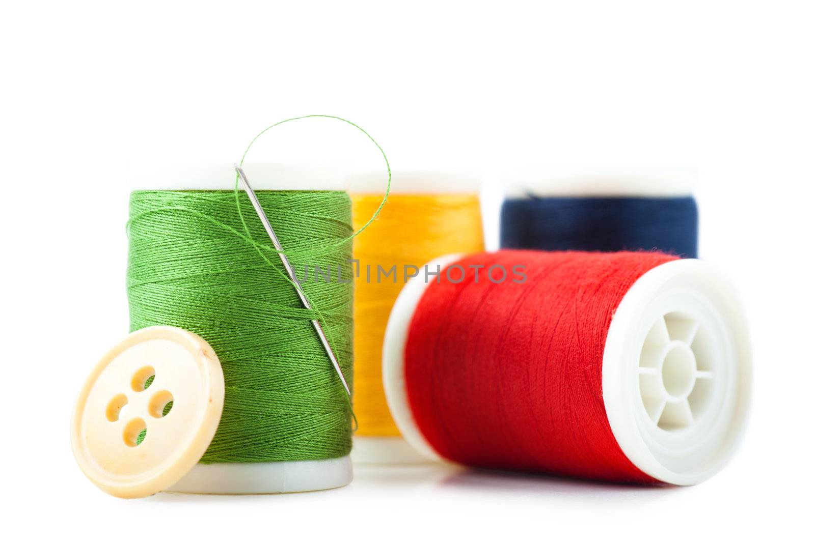 Four spools with green, red, yellow and blue threads, needle and button