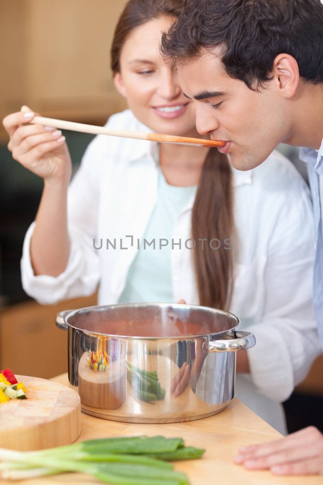 Portrait of a young man trying his wife's sauce in their kitchen