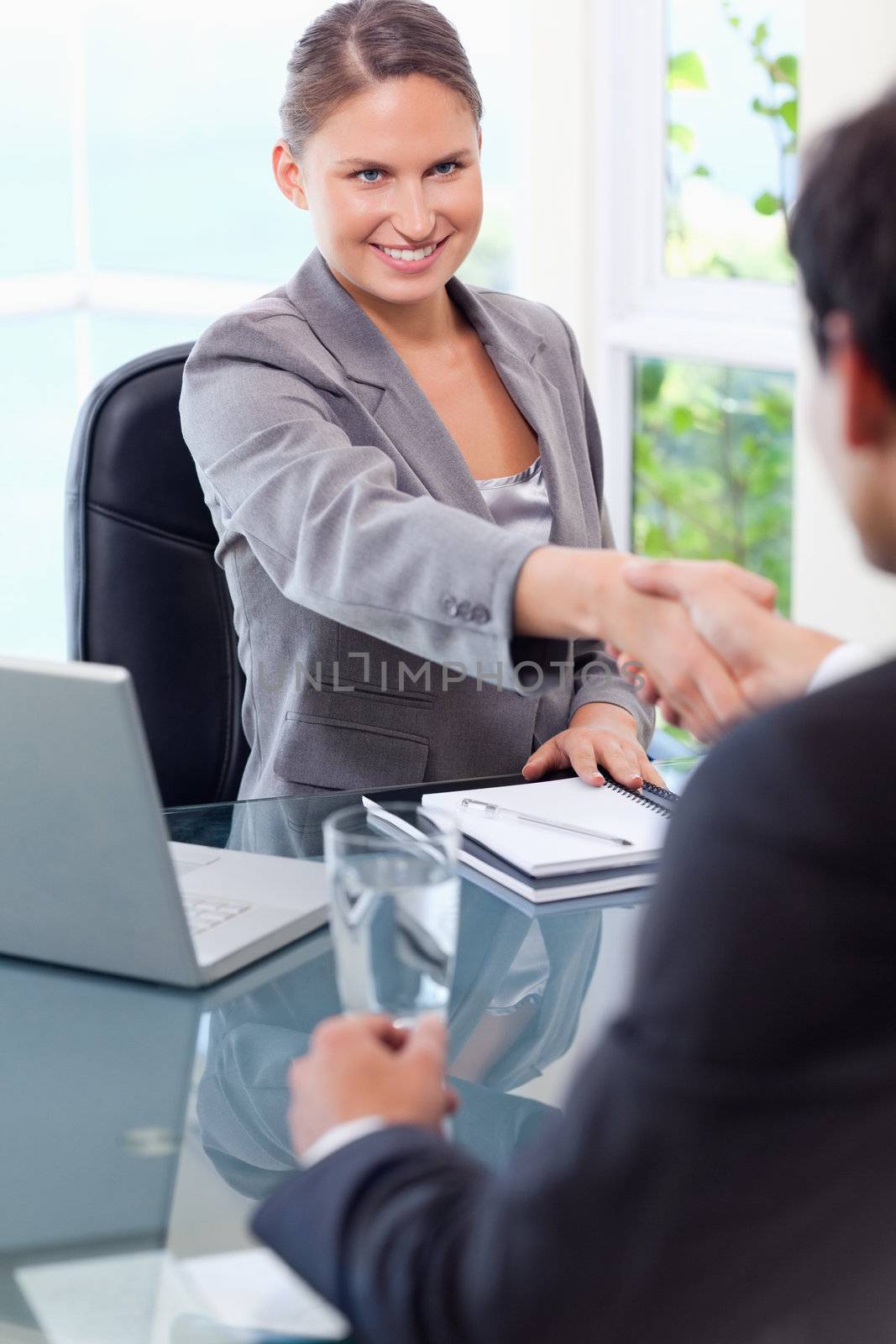 Smiling young businesswoman welcomes customer in her office