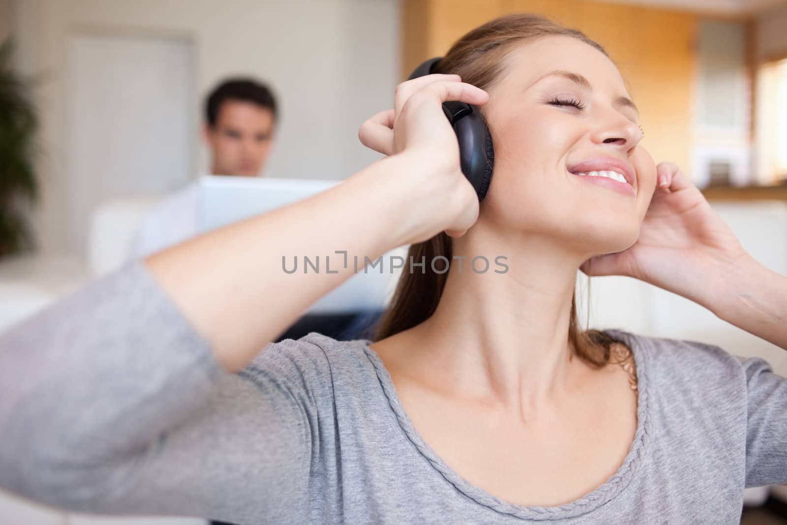 Young woman enjoying music with man sitting behind her on the sofa