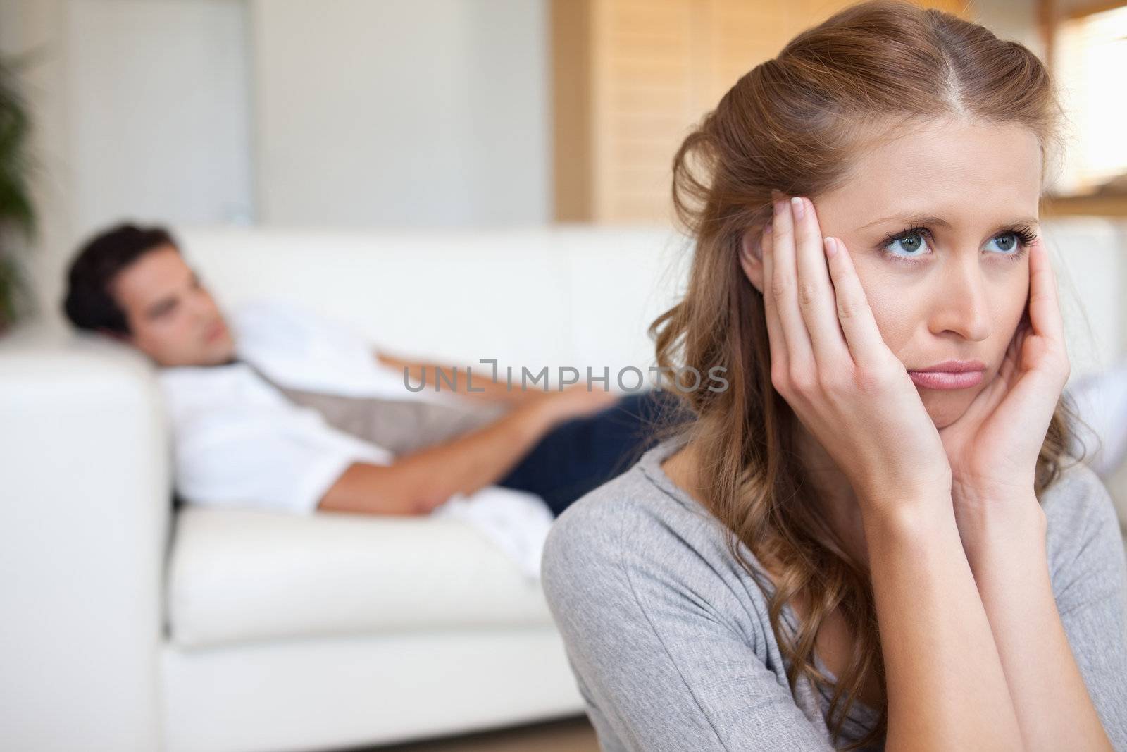 Sad looking young woman with man on the couch behind her