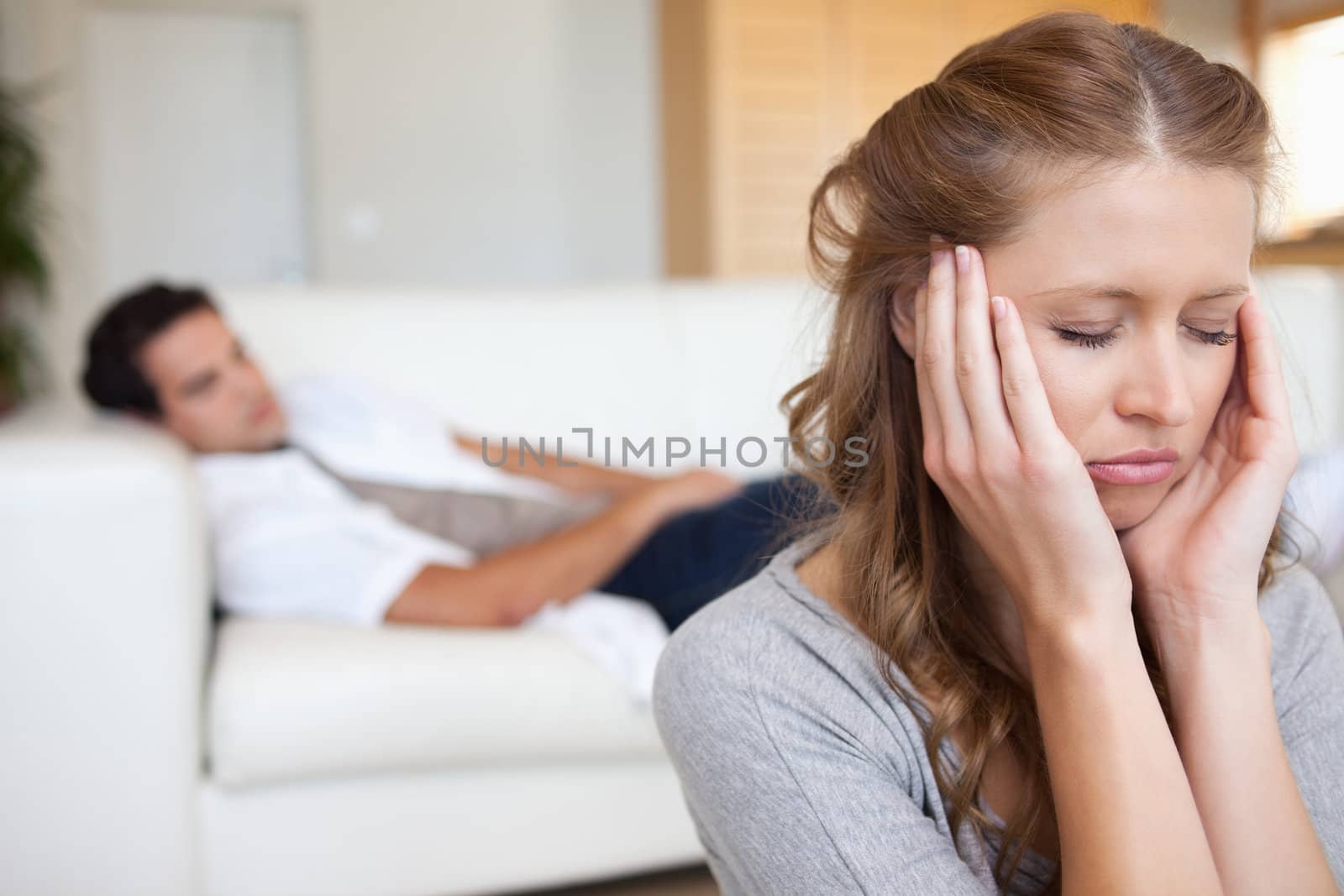 Young woman experiencing headache with man on the sofa behind her