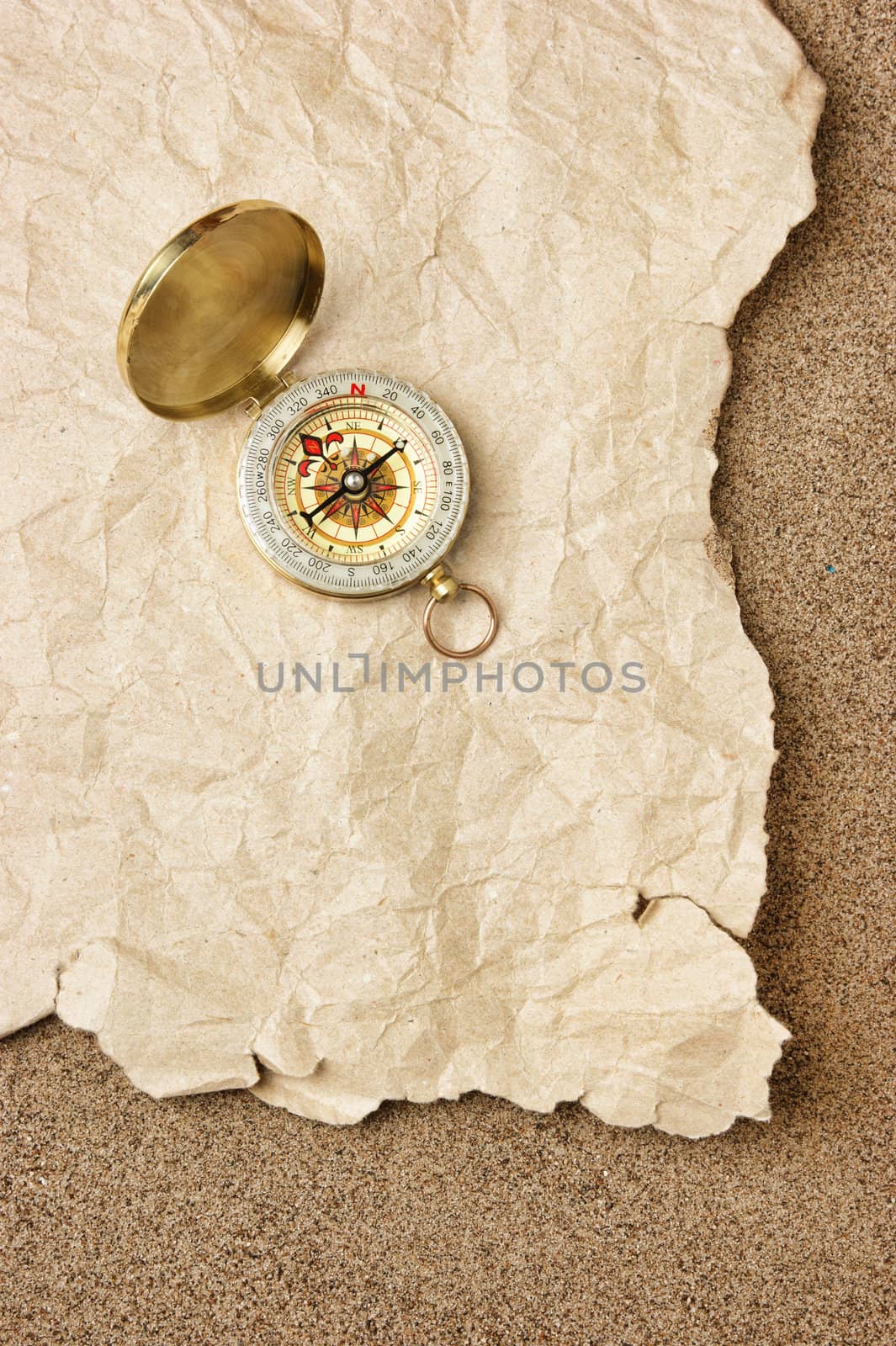 Compass on old sheet crumpled paper against the background of sand