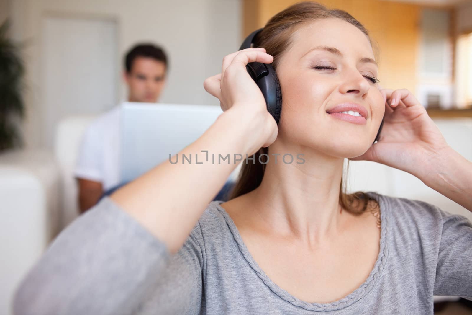 Young woman listening to music with man sitting behind her on the sofa