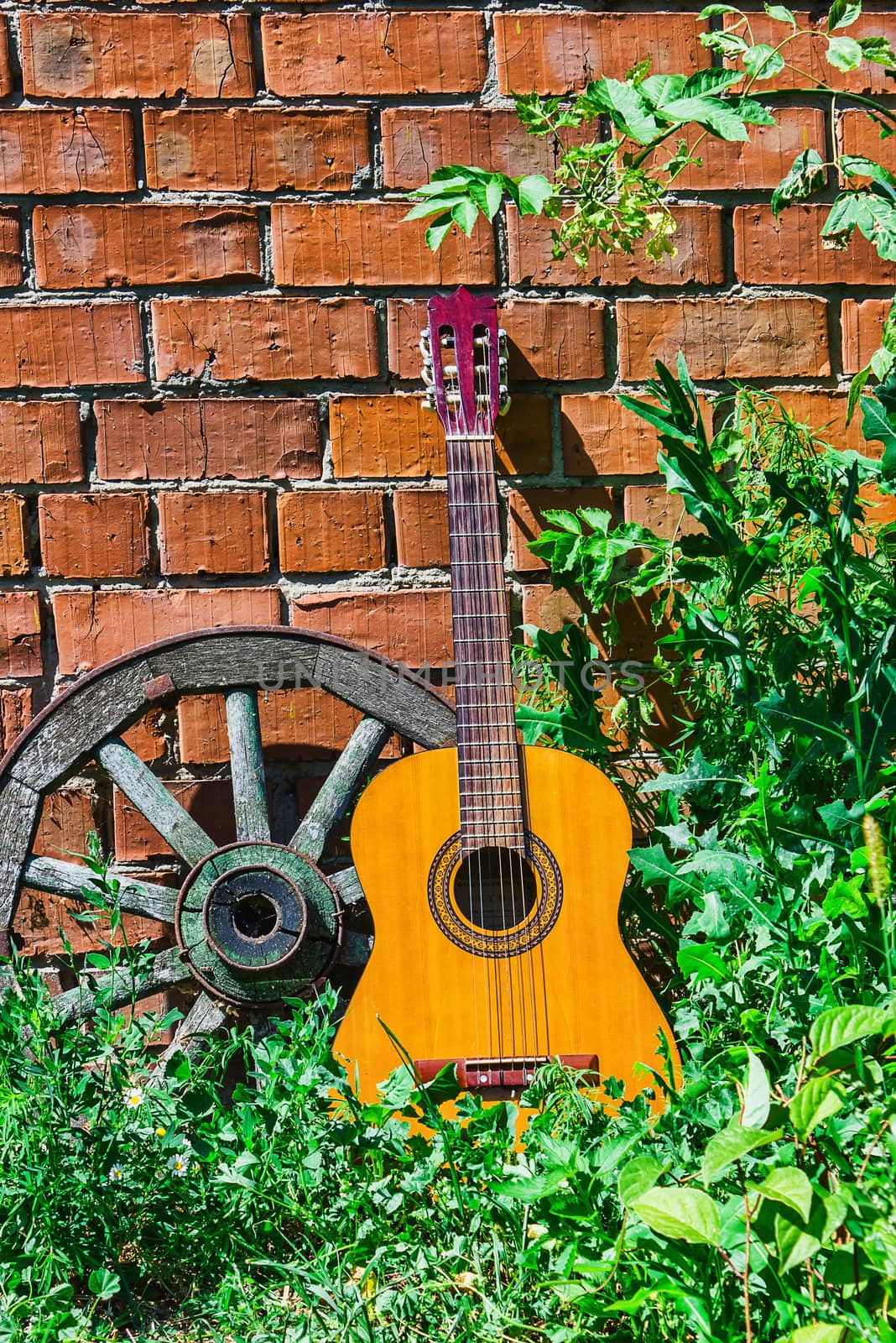 Guitar and the old wagon wheel against a brick wall