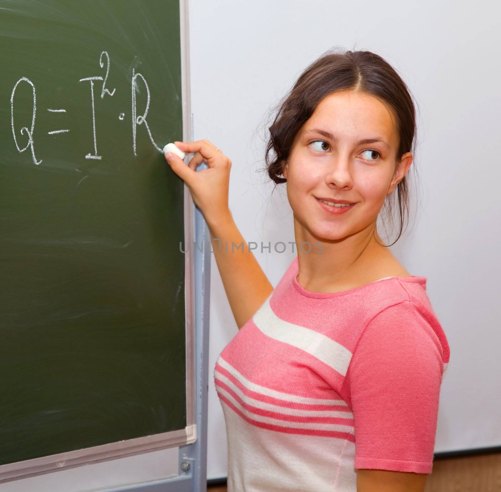 Beautiful girl in a physics class writes the formula on the blackboard