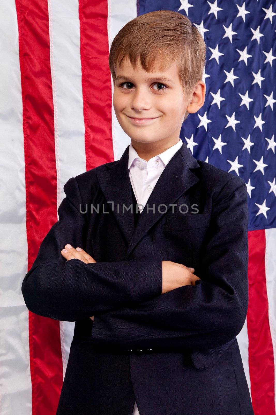 Portait of Caucasian boy with arms crossed with American flag in background.