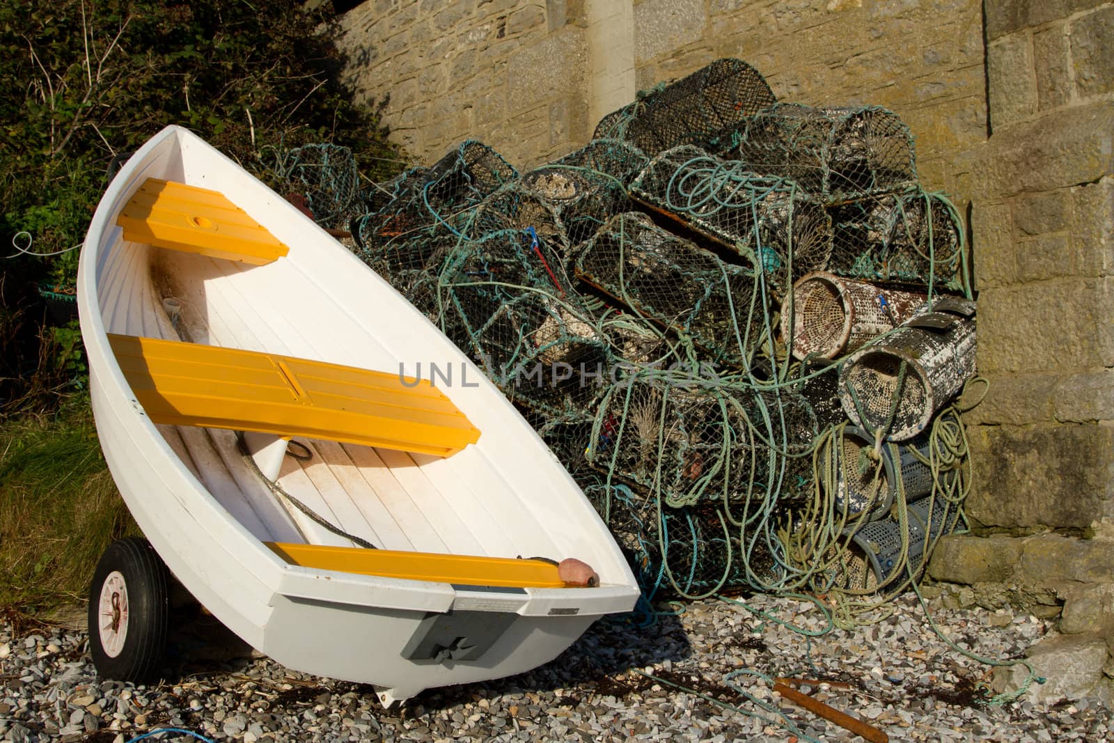 A white boat, dinghy, out of water next to a pile of lobster and crab pots.