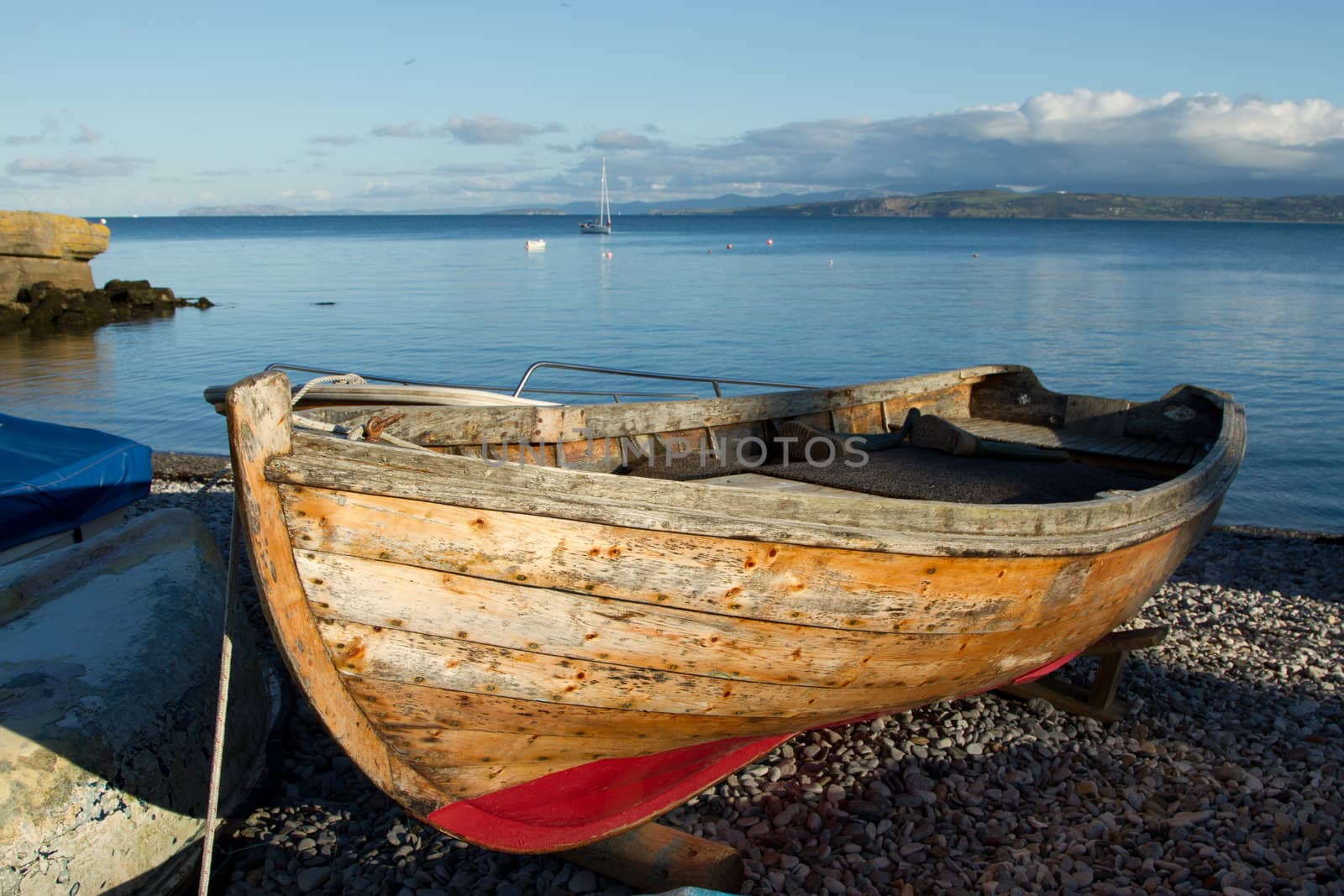 A wooden boat out of water on a pebble beach with the sea and blue sky in the distance