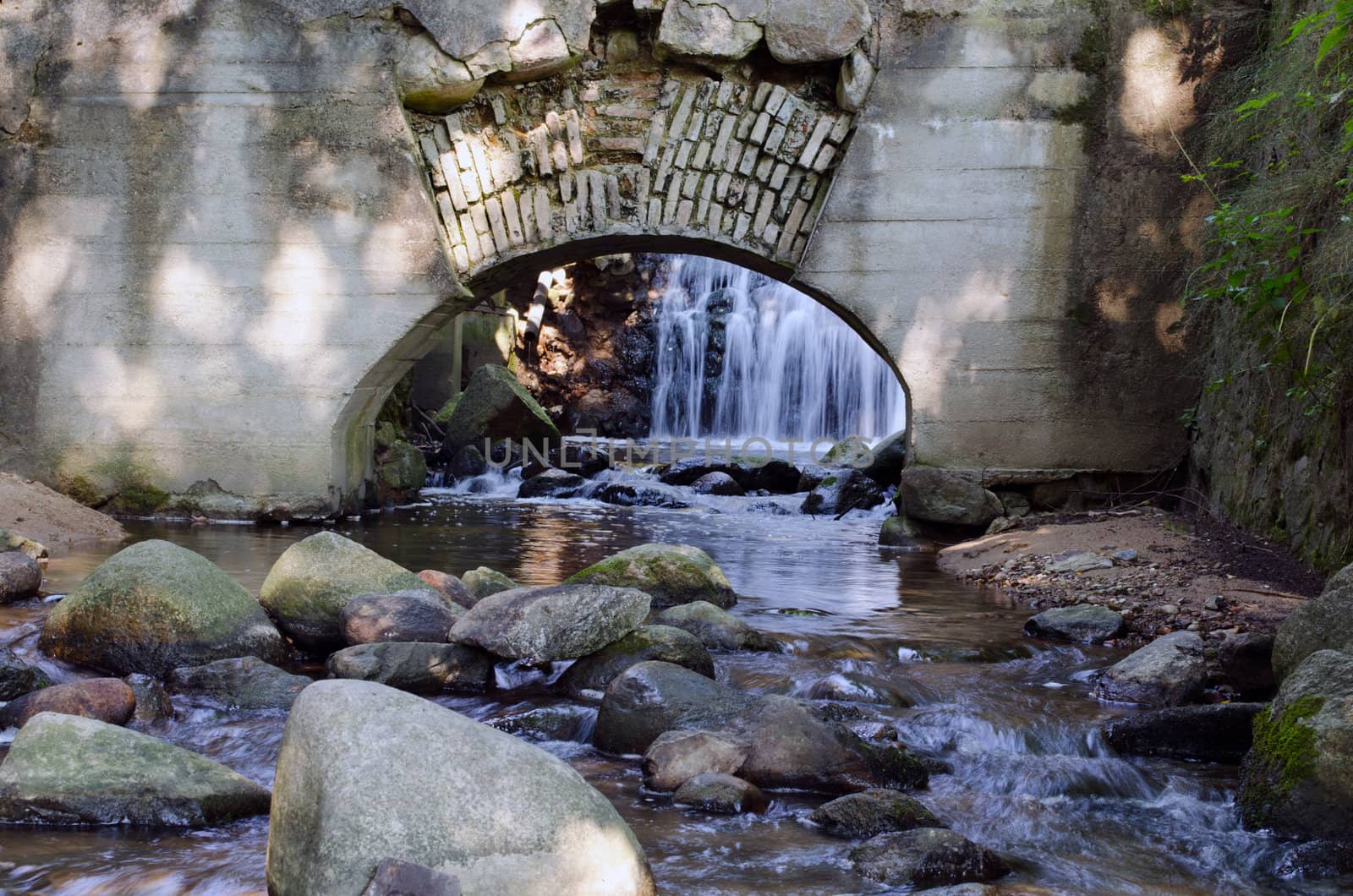 Retro architecture arch in wall and stream flowing from waterfall.