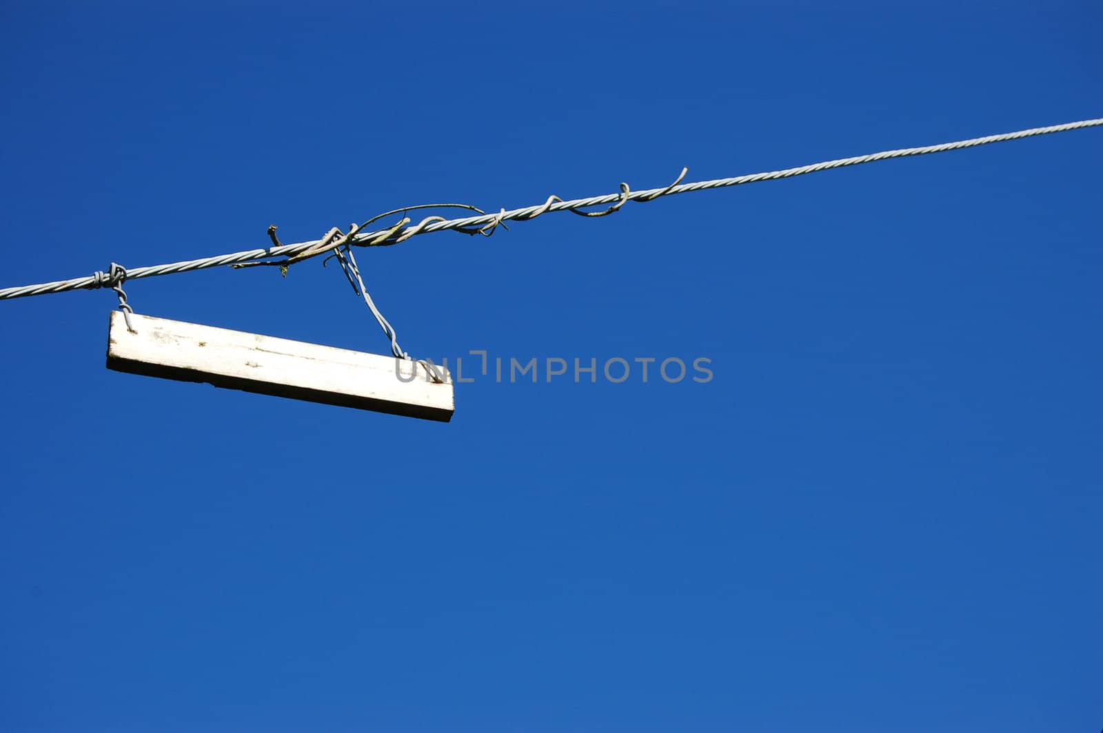 Plain white sign hung on a twisted metal cable against a blue sky