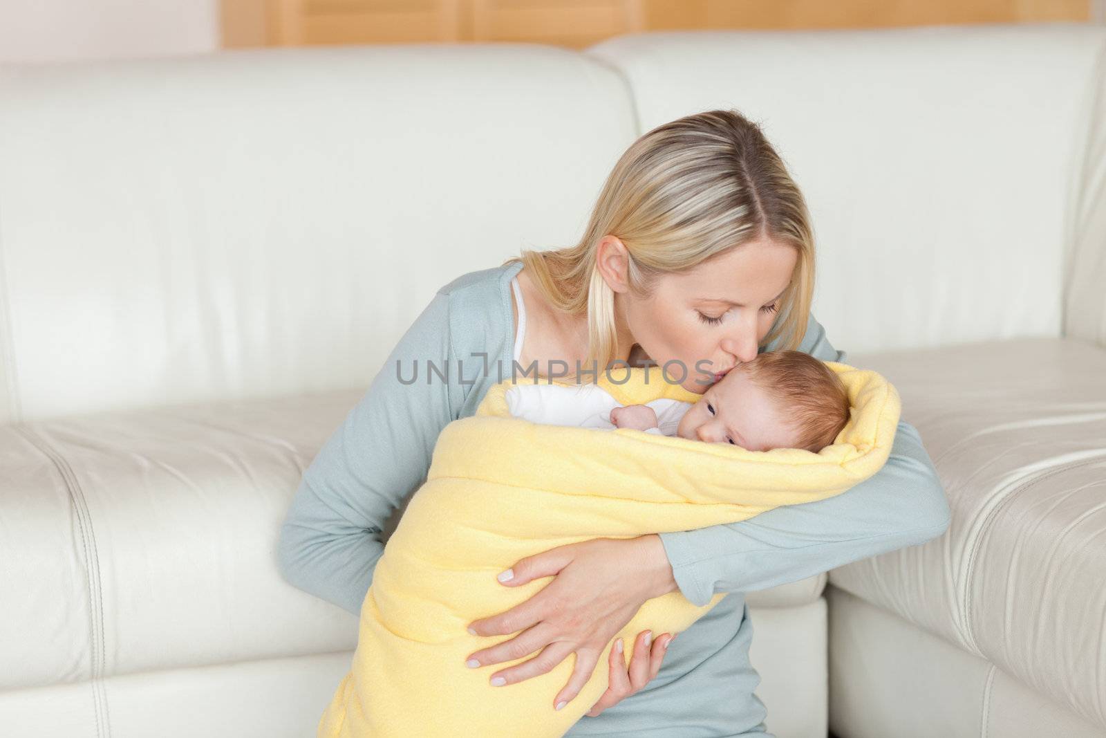 Lovely young mother kissing her baby which is wrapped into a cover