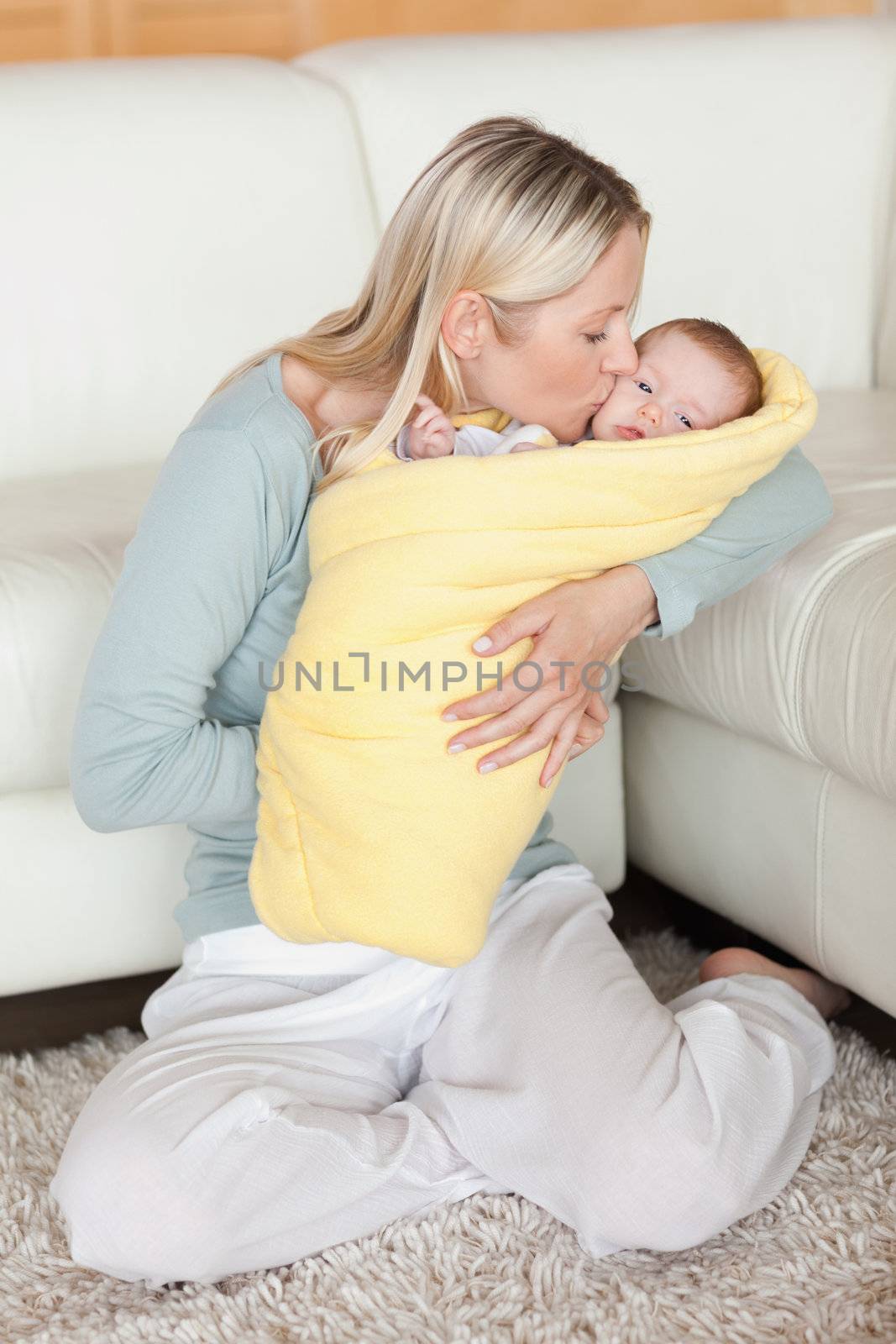 Young mom kissing her baby that is wrapped into a cover