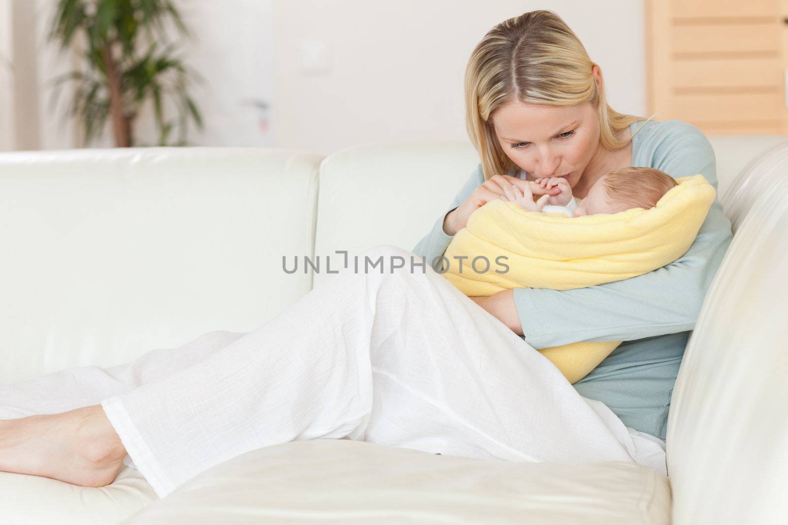 Young mother sitting on the couch kissing her baby in her arms