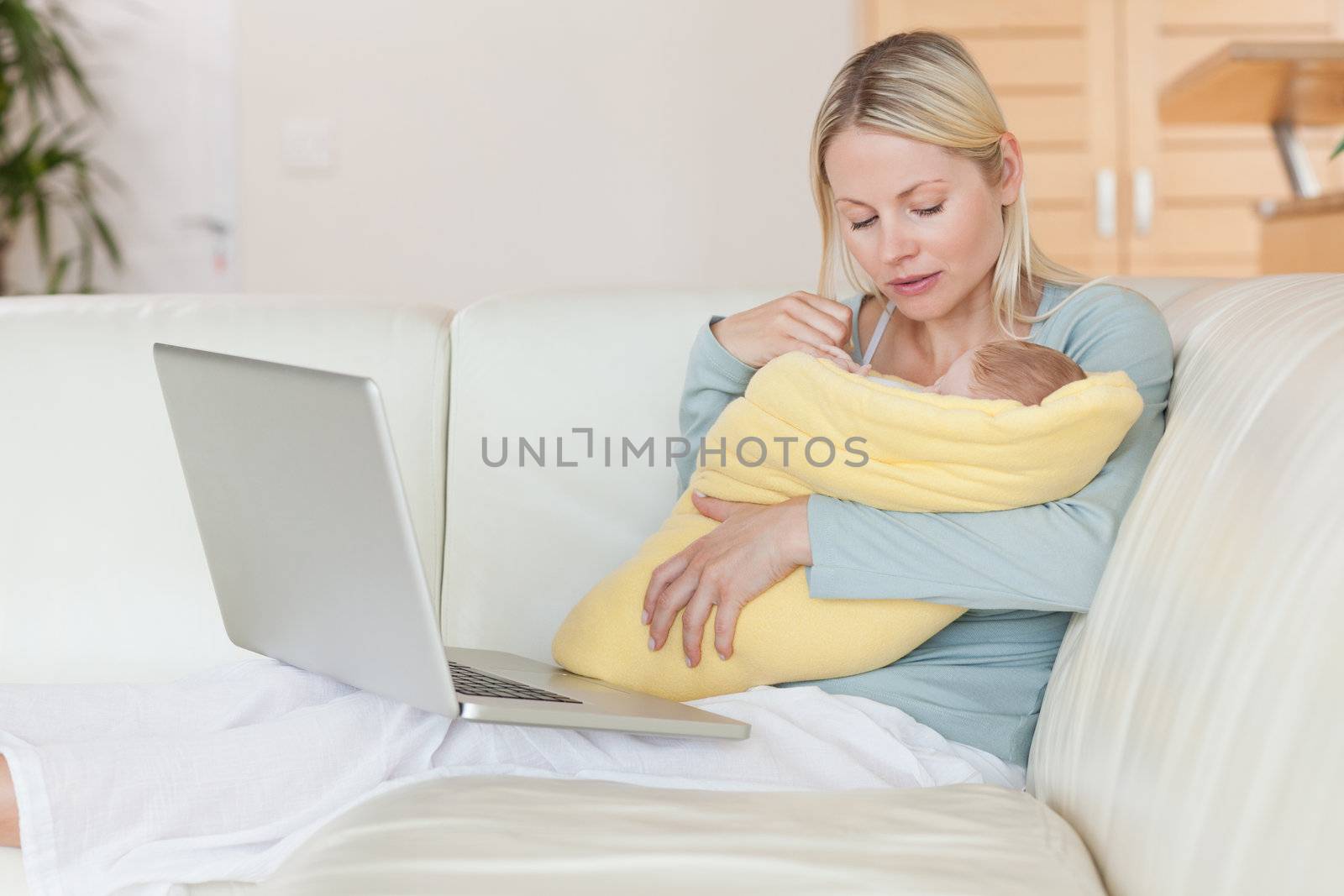 Young mother with notebook on the sofa holding her baby