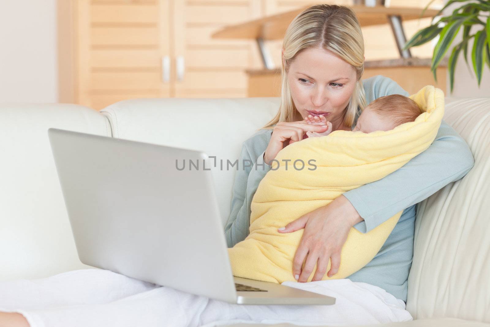 Young mother holding her baby while looking at her laptop