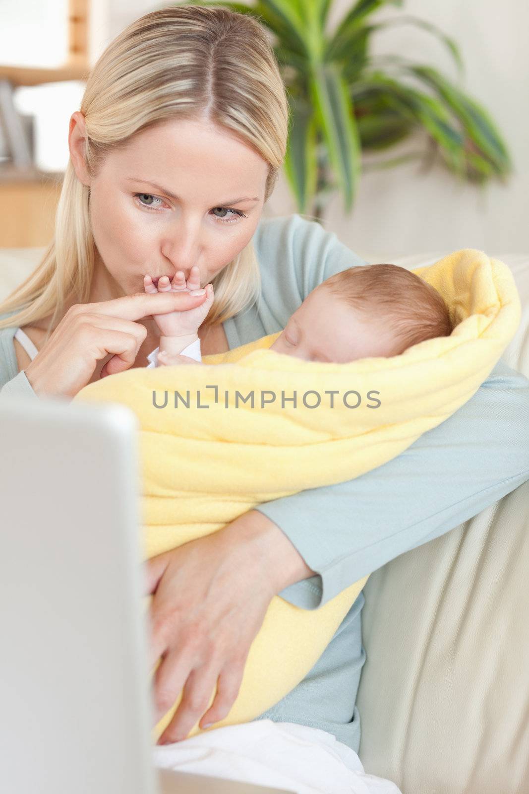 Young mother kissing her baby's hand while looking at the laptop