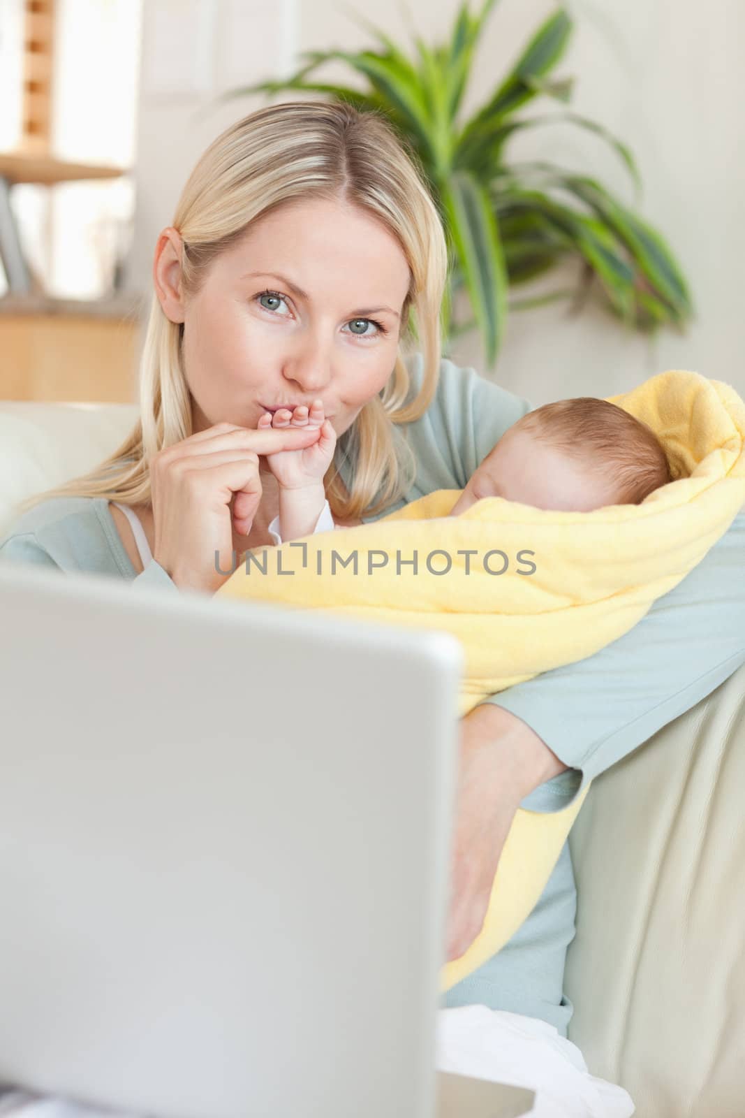 Young mother kissing her baby's hand while sitting on the sofa
