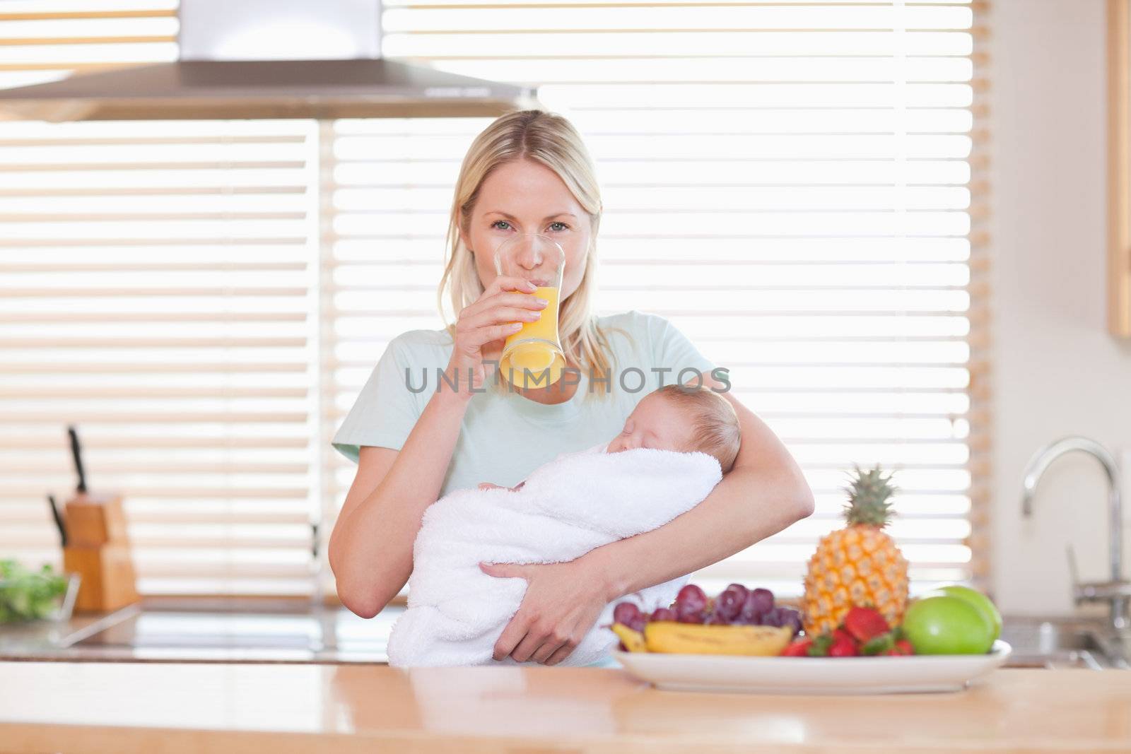 Woman drinking orange juice while holding her baby