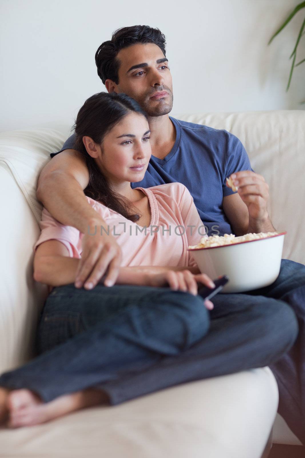 Portrait of a couple watching television while eating popcorn in their living room