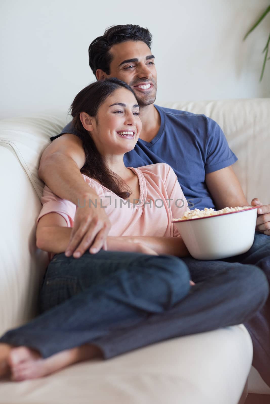 Portrait of a happy couple watching television while eating popcorn in their living room