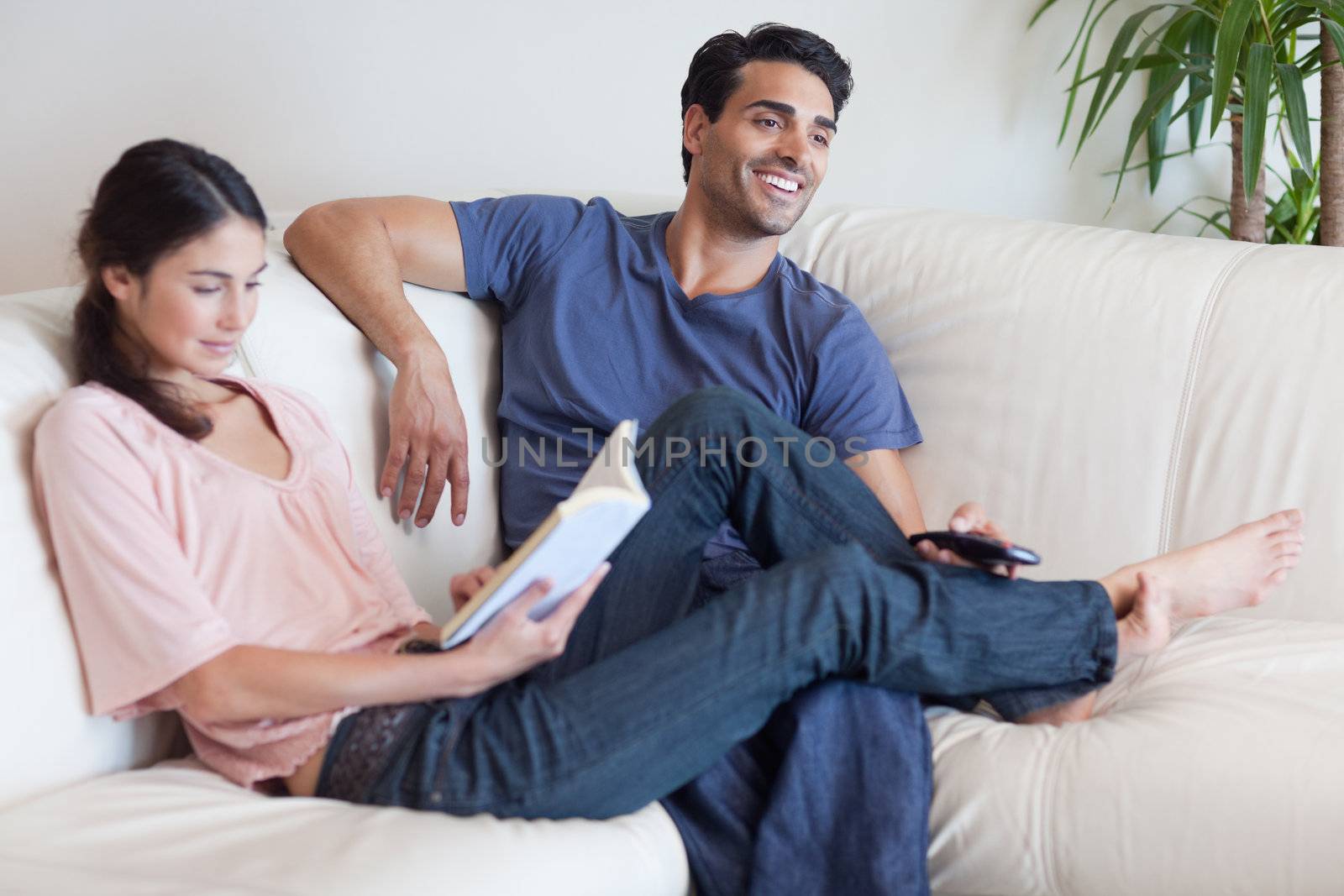 Woman reading a book while her husband is watching television in their living room