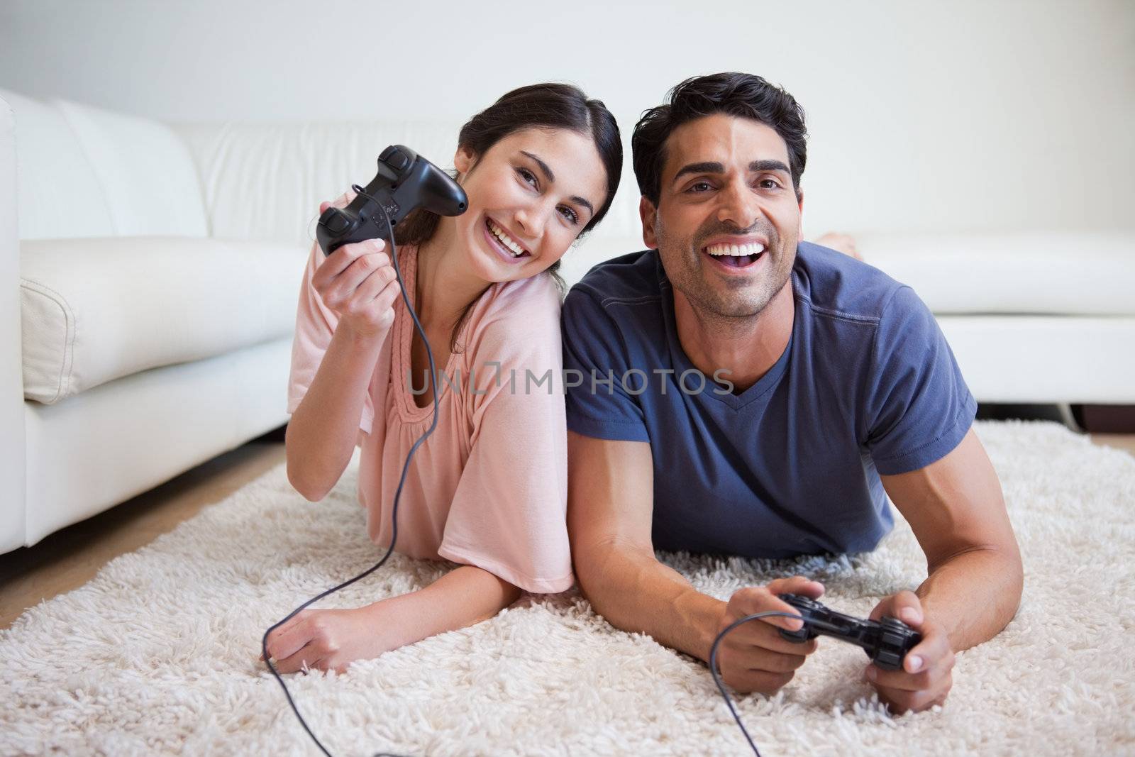 Delighted couple playing video games while lying on a carpet