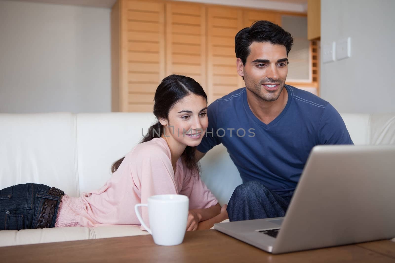 Young couple using a laptop while having a coffee in their living room