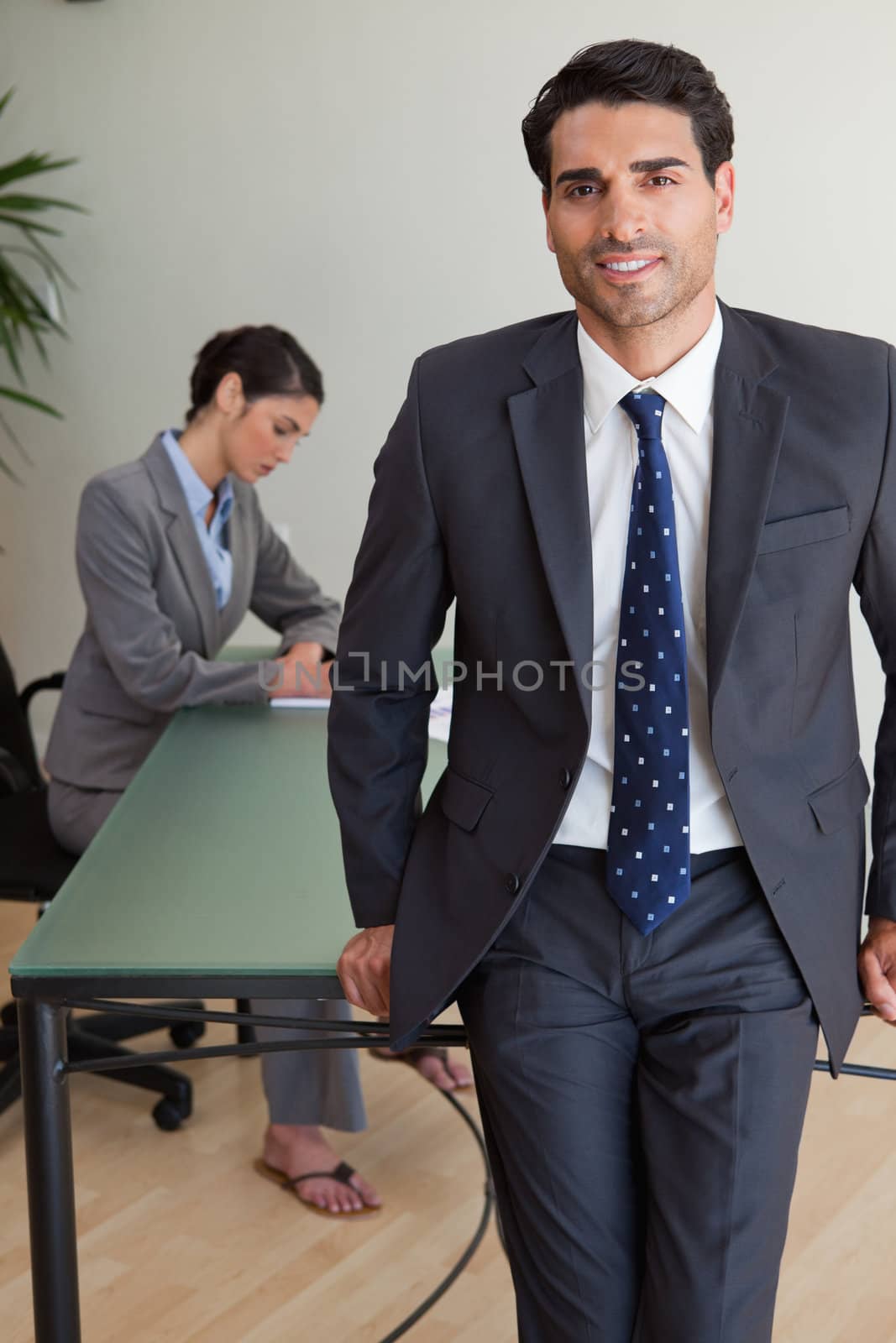 Portrait of a handsome businessman posing while his colleague is working in an office