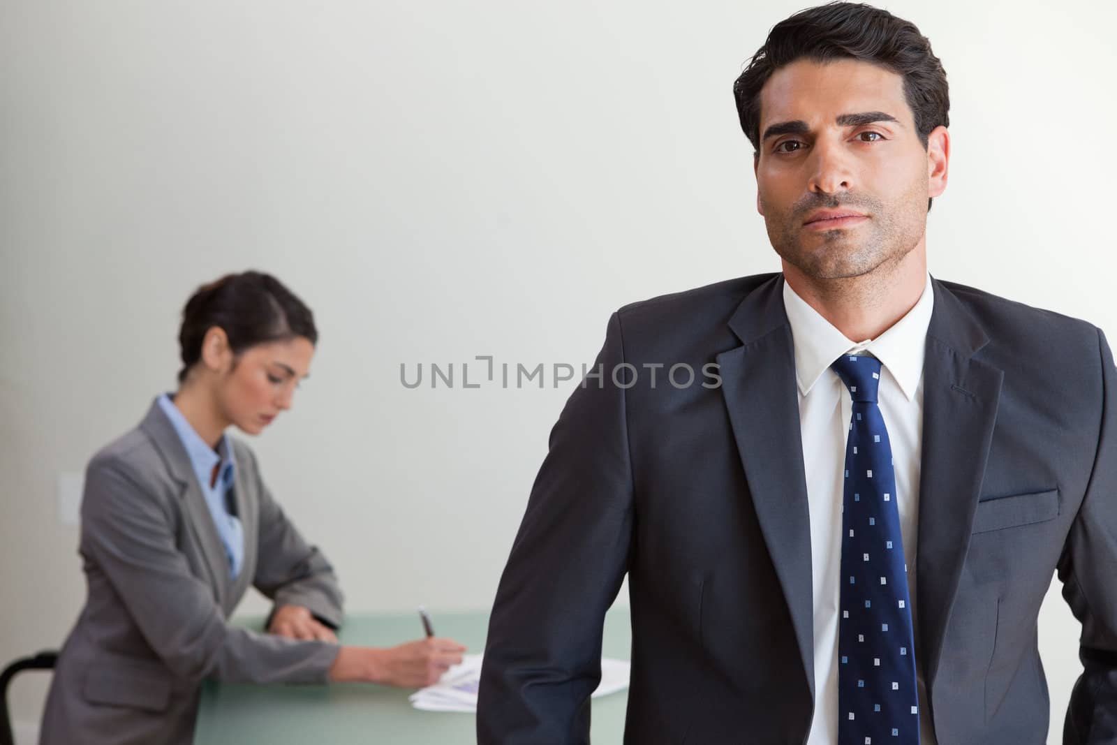 Handsome businessman posing while his colleague is working in an office