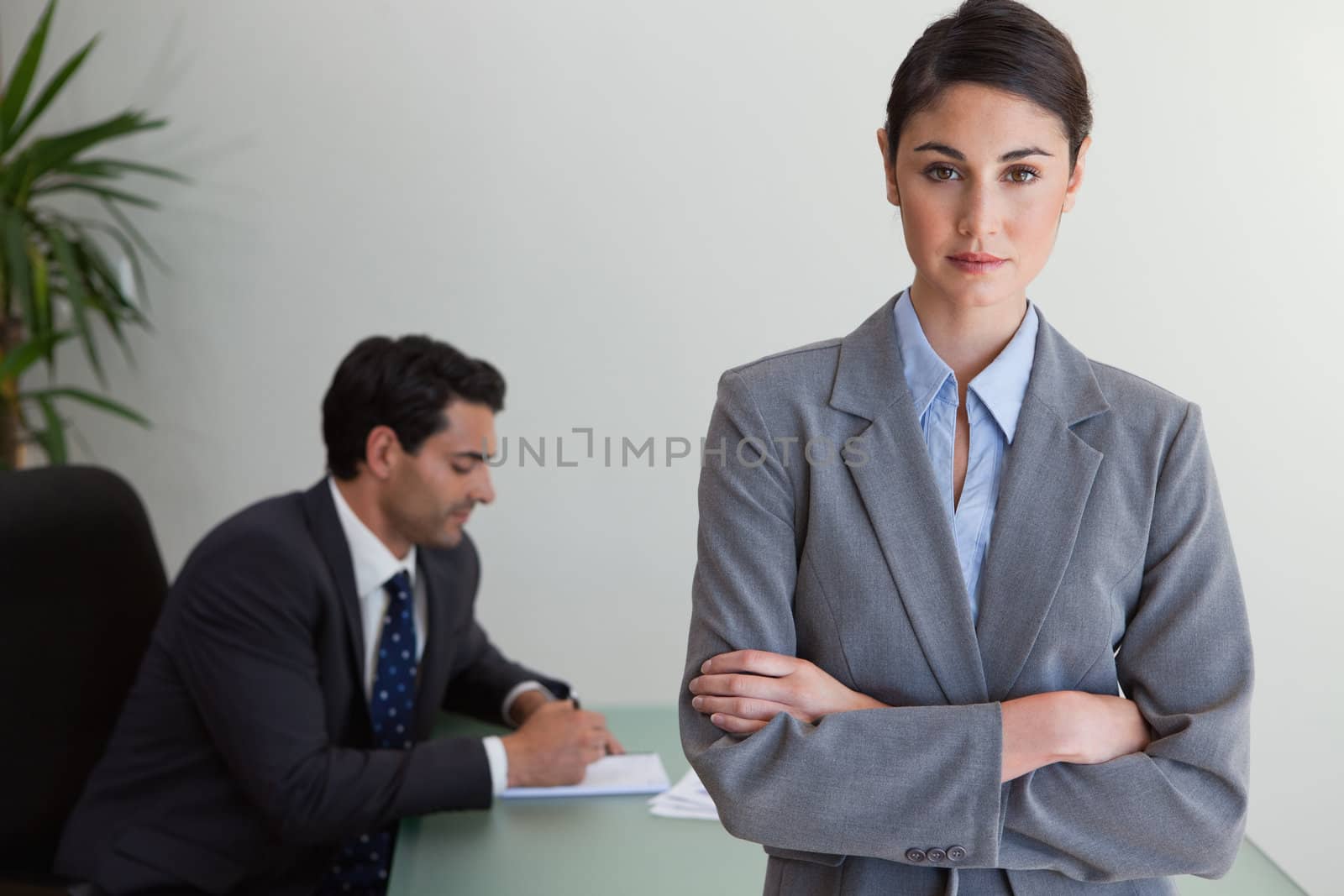 Professional businesswoman posing while her colleague is working in an office