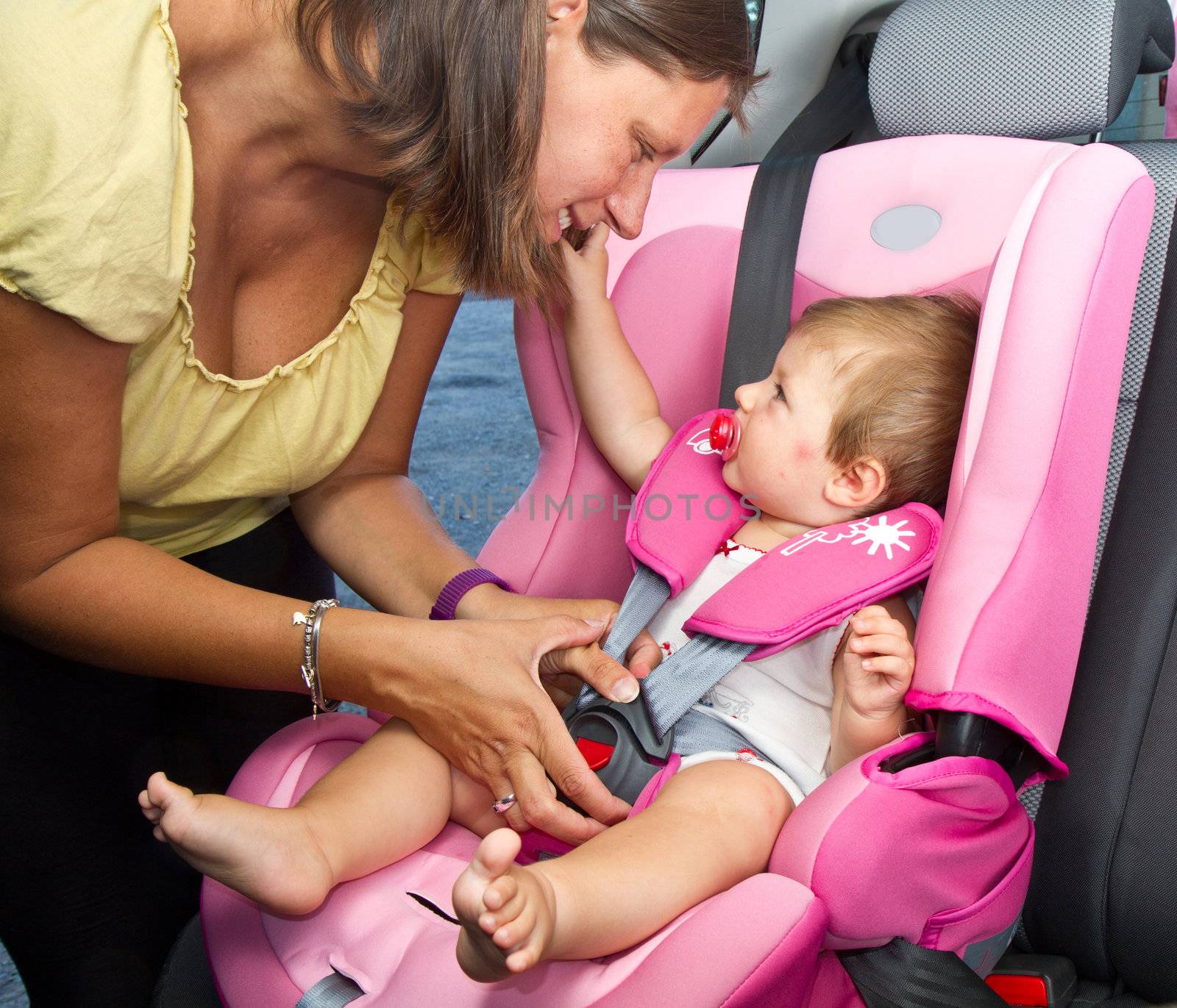 Woman fastening her son on a baby seat in a car 