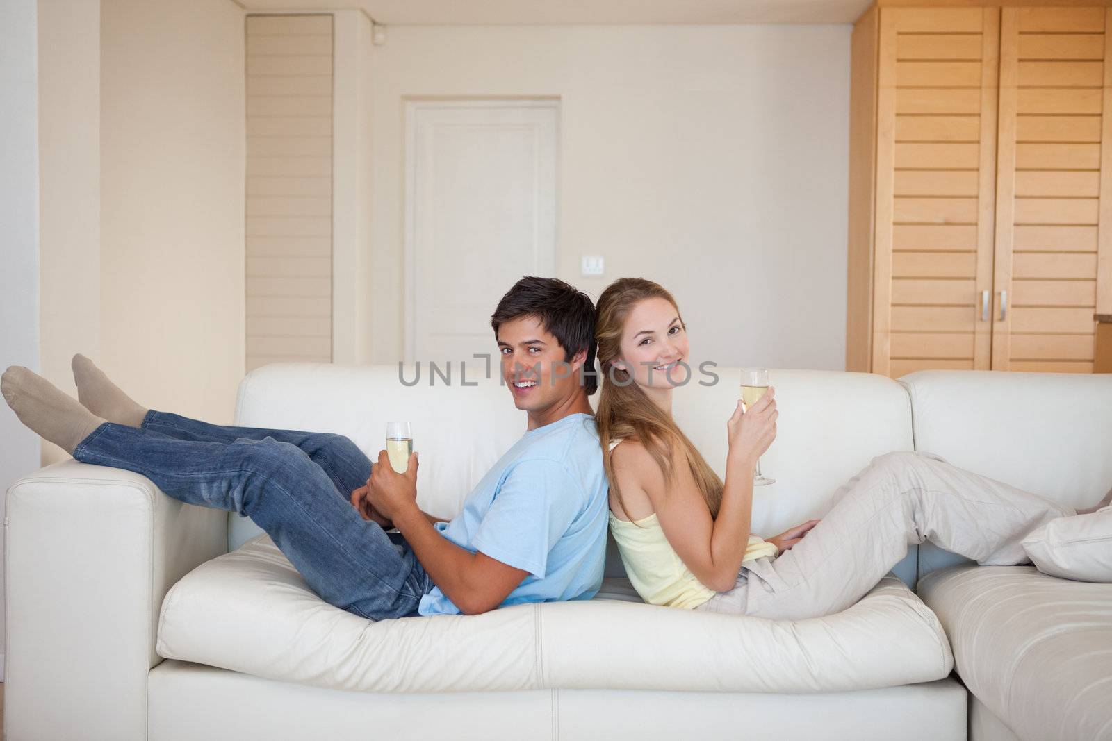 Couple sitting back to back while drinking sparkling wine in their living room