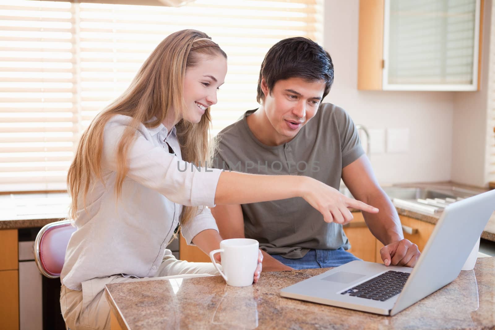 Smiling couple having coffee while using a laptop in their kitchen