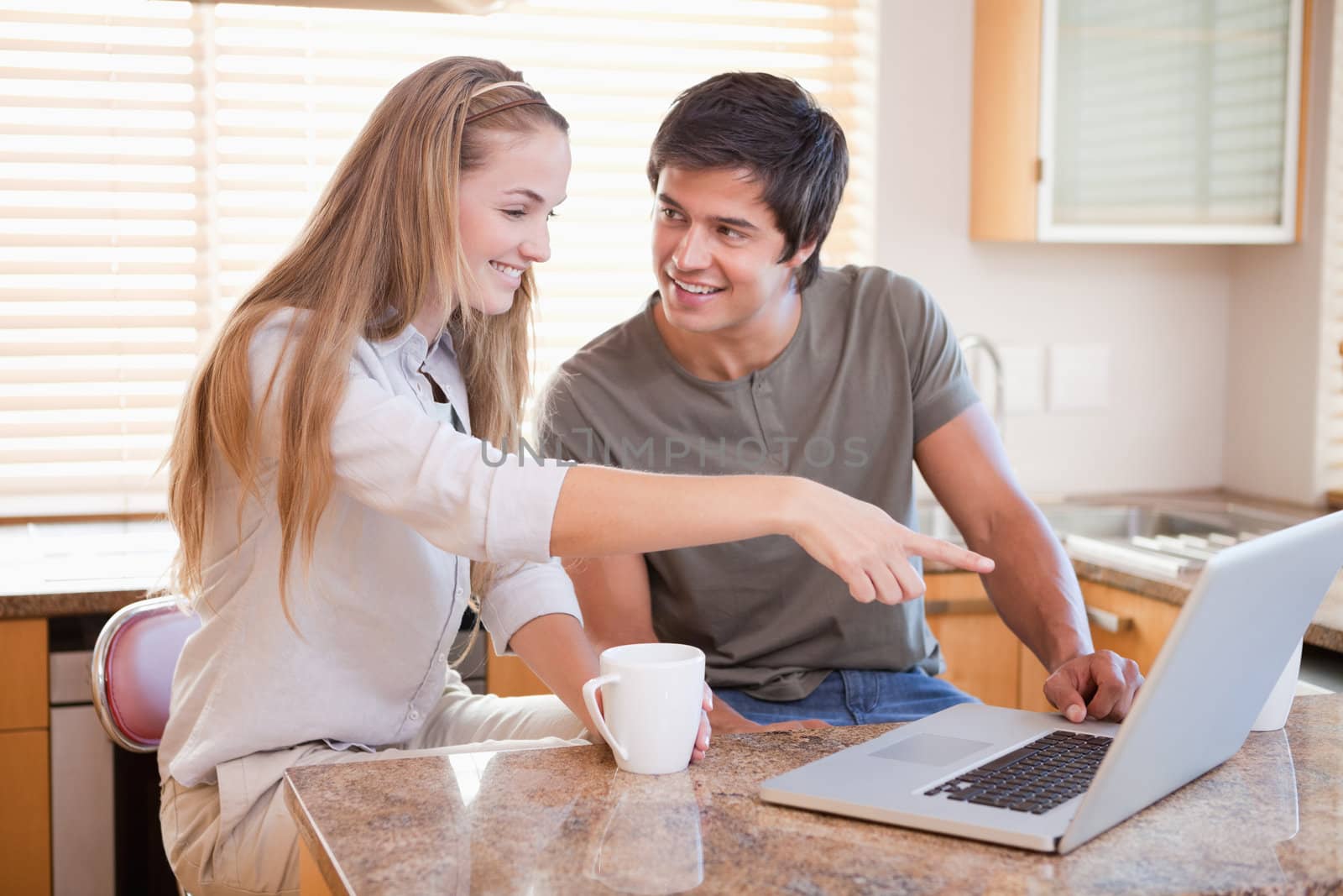 Smiling couple having coffee while using a notebook in their kitchen