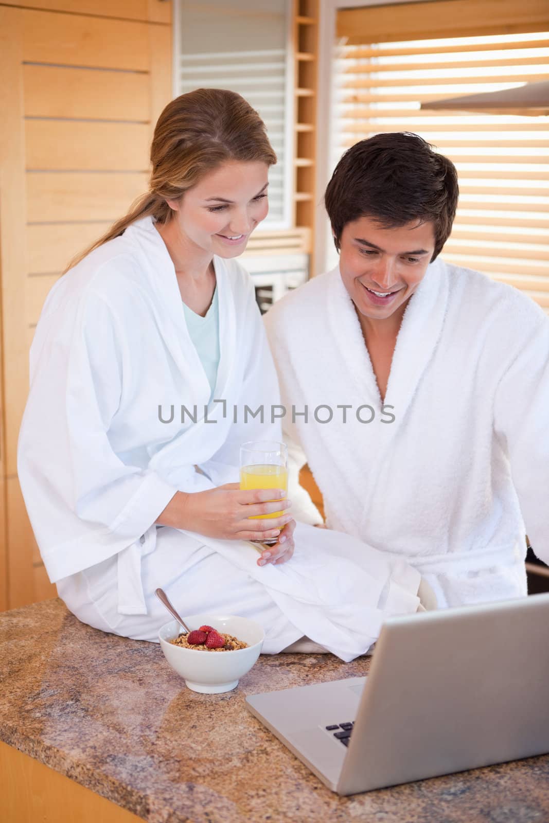 Portrait of a young couple having breakfast while using a laptop in their kitchen