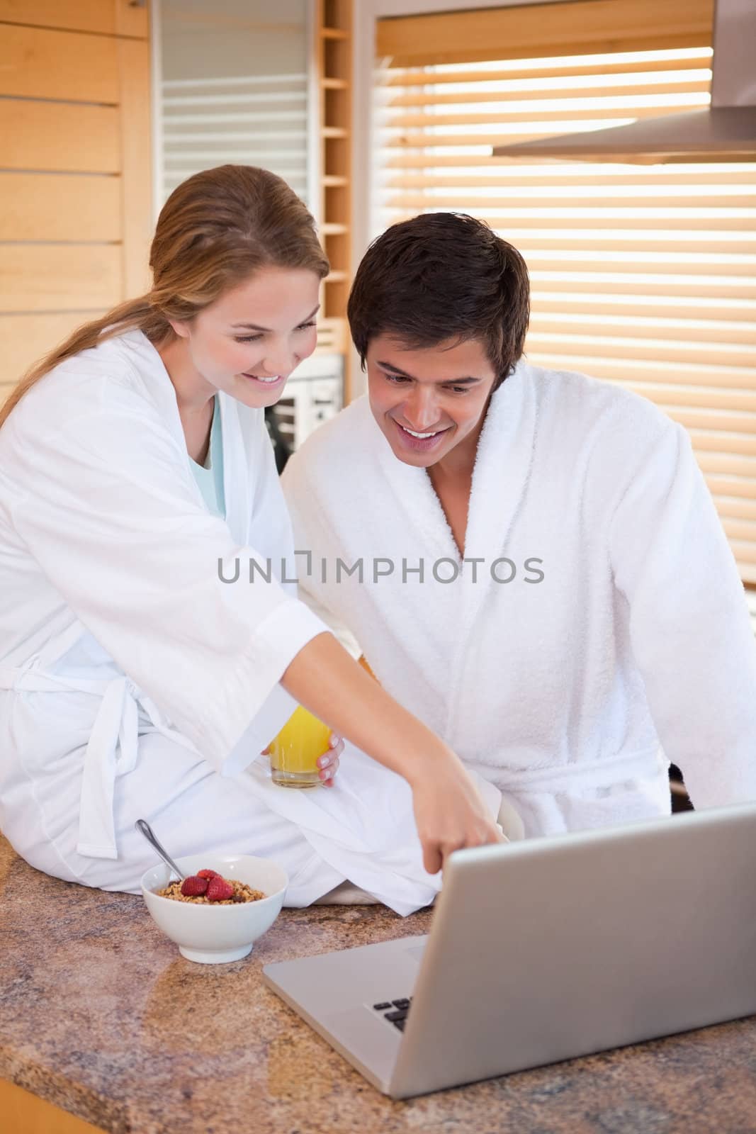 Portrait of a lovely couple having breakfast while using a laptop in their kitchen