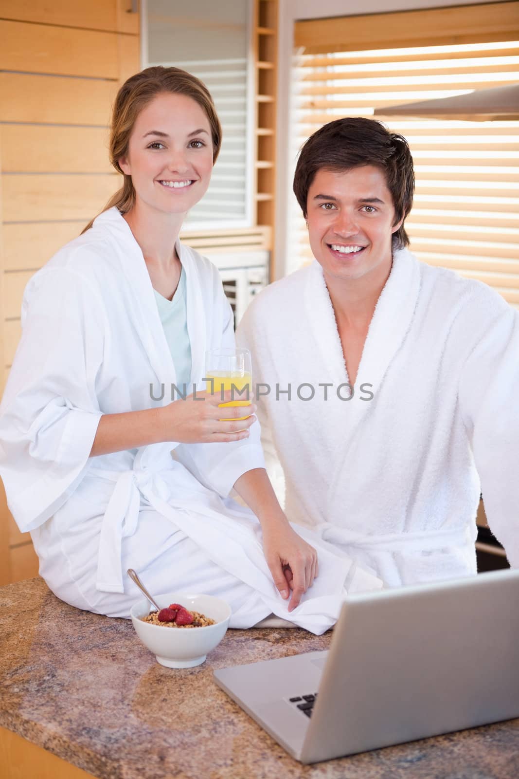 Portrait of a charming couple having breakfast while using a notebook in their kitchen