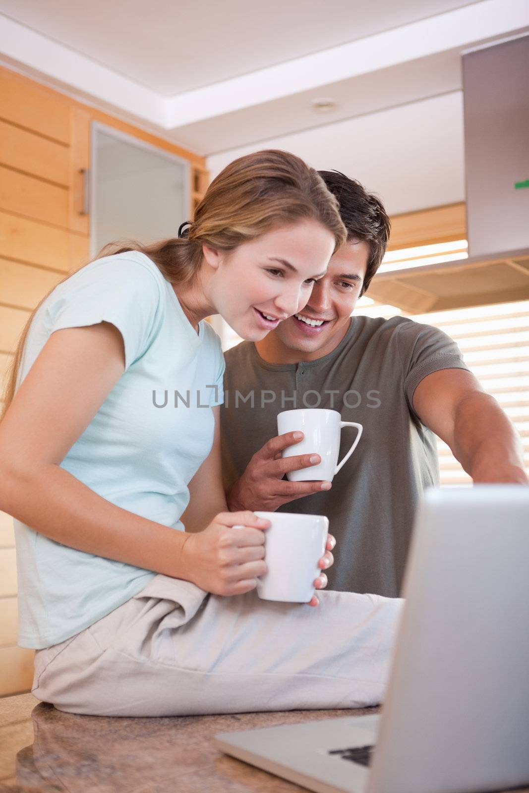 Portrait of a young couple having tea while using a laptop in their kitchen