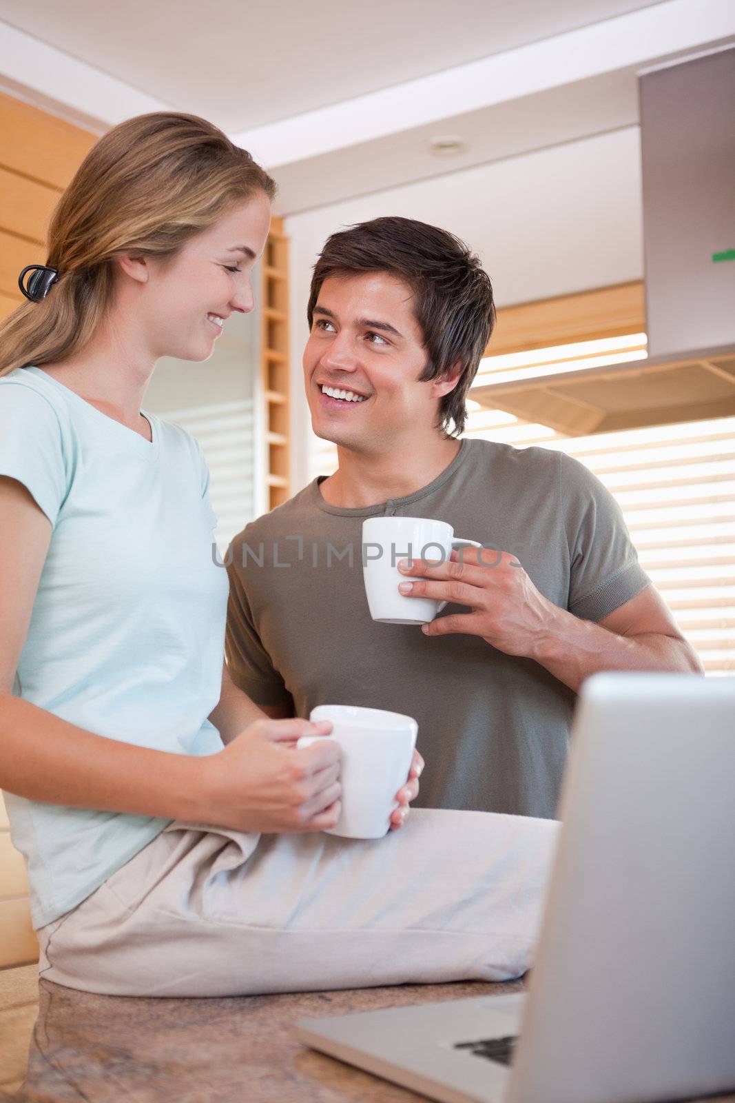 Portrait of a young couple having coffee while using a notebook in their kitchen