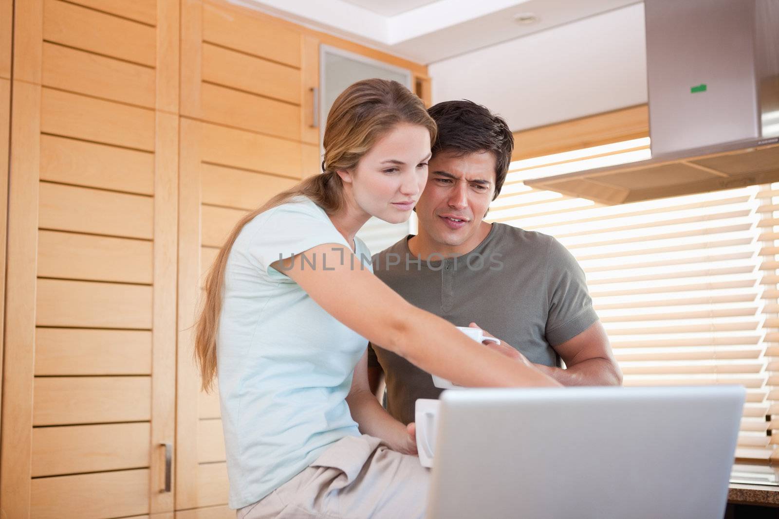Young couple having tea while using a laptop in their kitchen