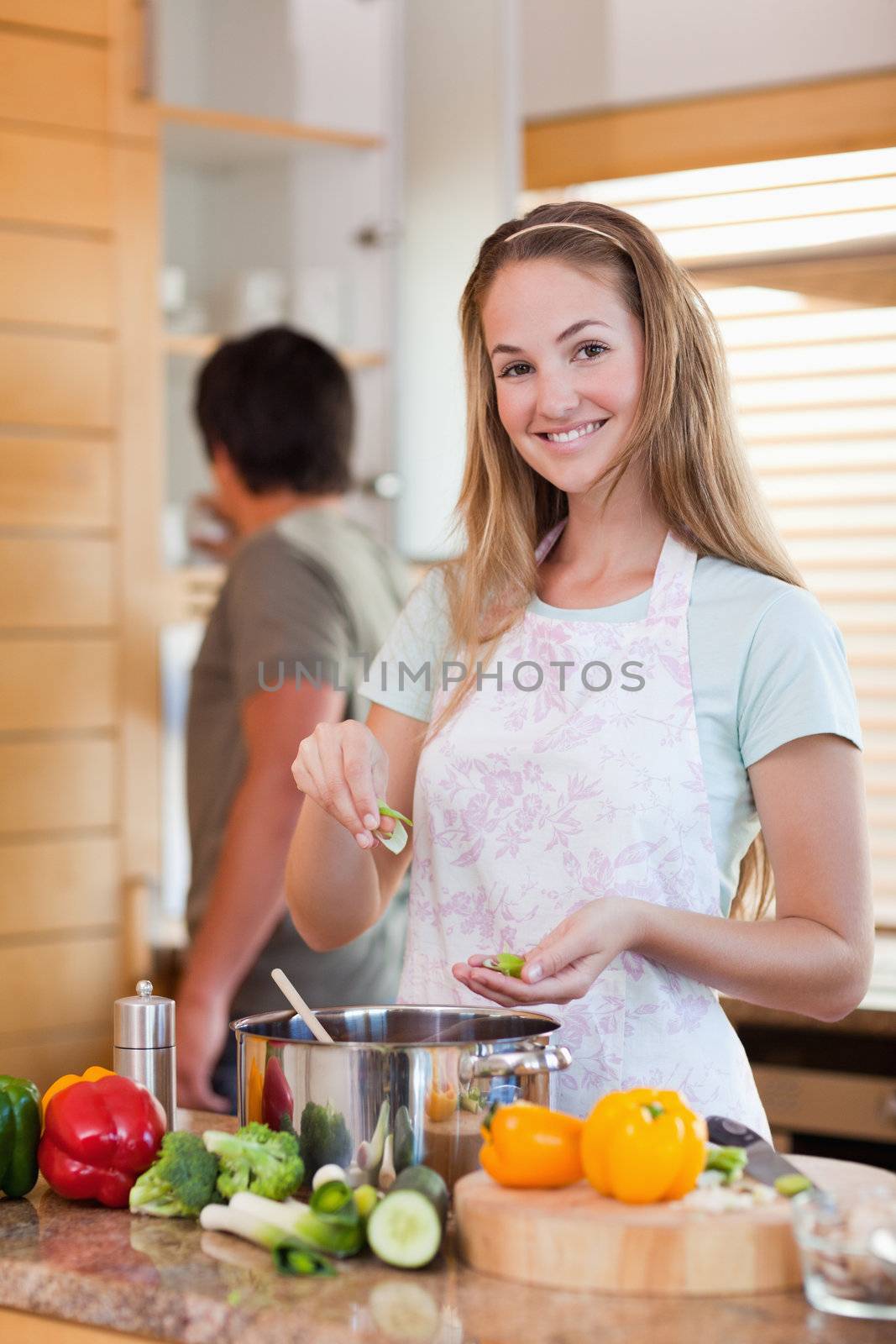Portrait of a woman cooking while her fiance is washing the dishes in their kitchen