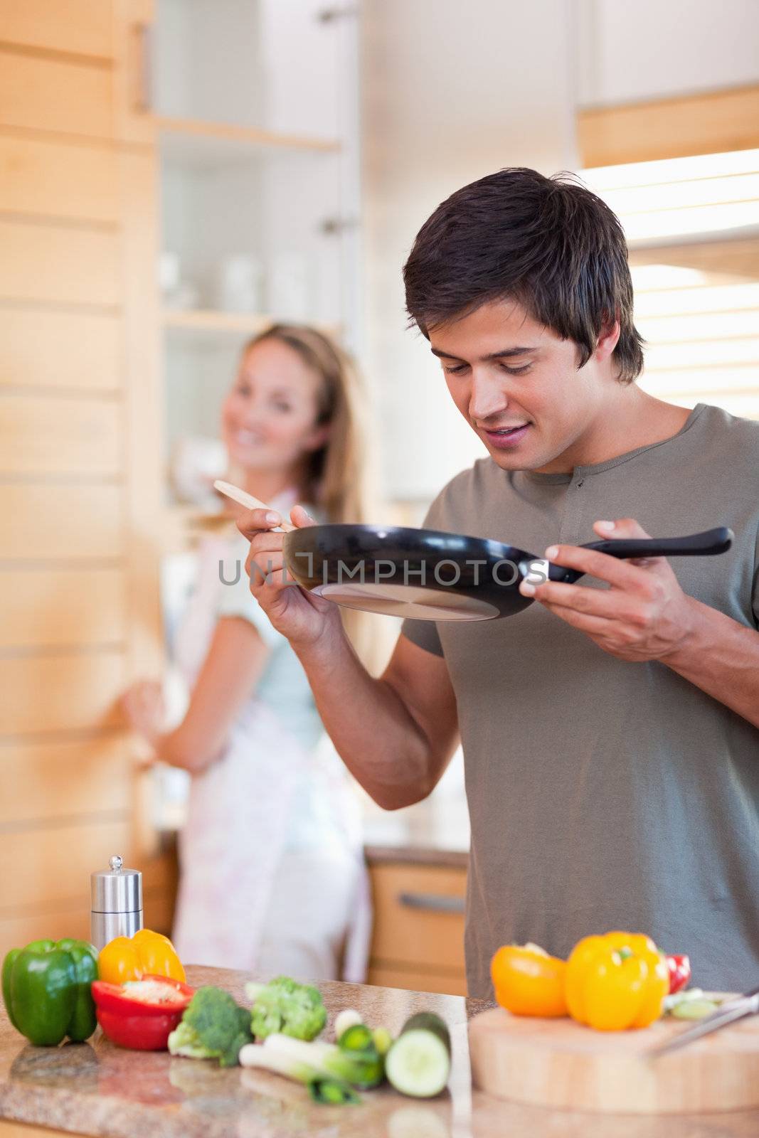 Portrait of a man cooking while his fiance is washing the dishes in their kitchen
