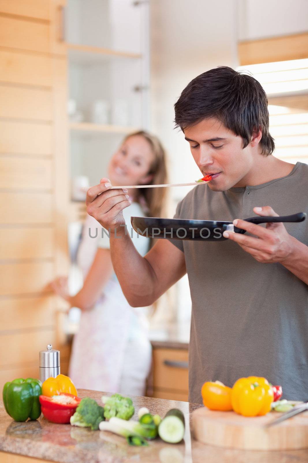 Portrait of a man cooking while his girlfriend is washing the dishes in their kitchen