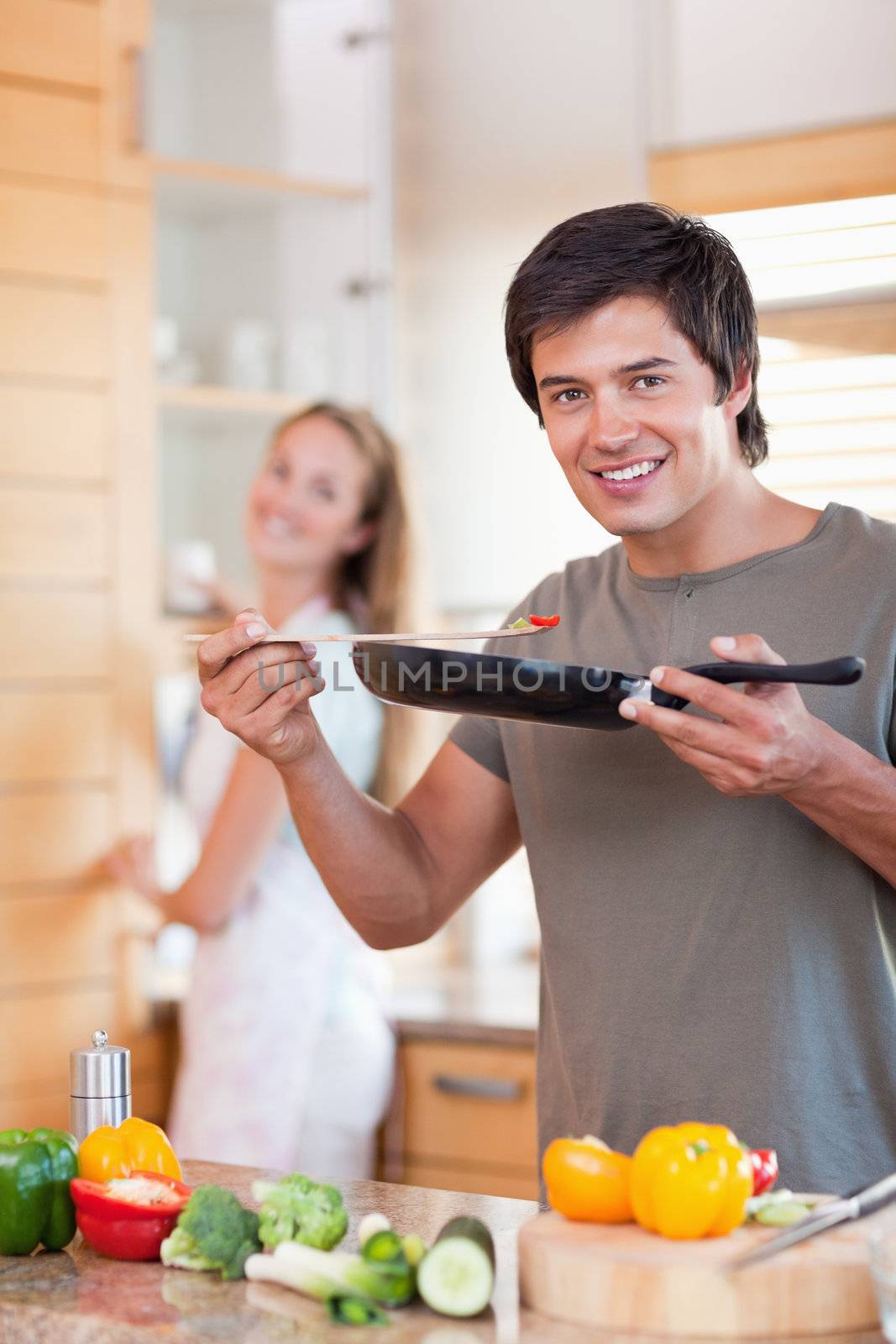 Portrait of a young man cooking while his wife is washing the dishes in their kitchen