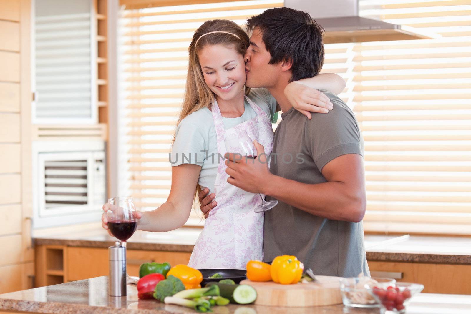 Lovely couple drinking red wine while kissing in their kitchen